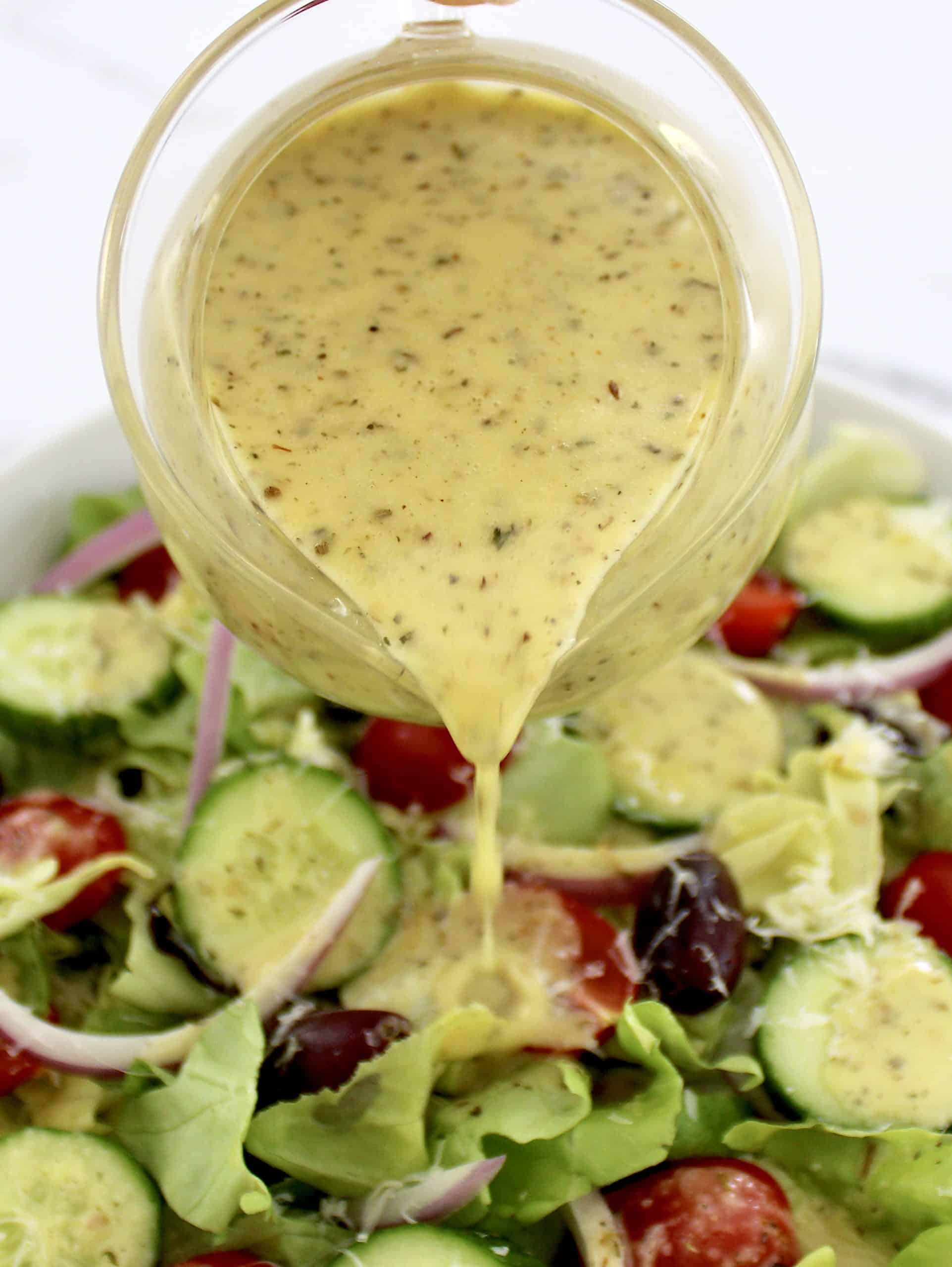 Homemade Italian Dressing being poured over salad from glass 