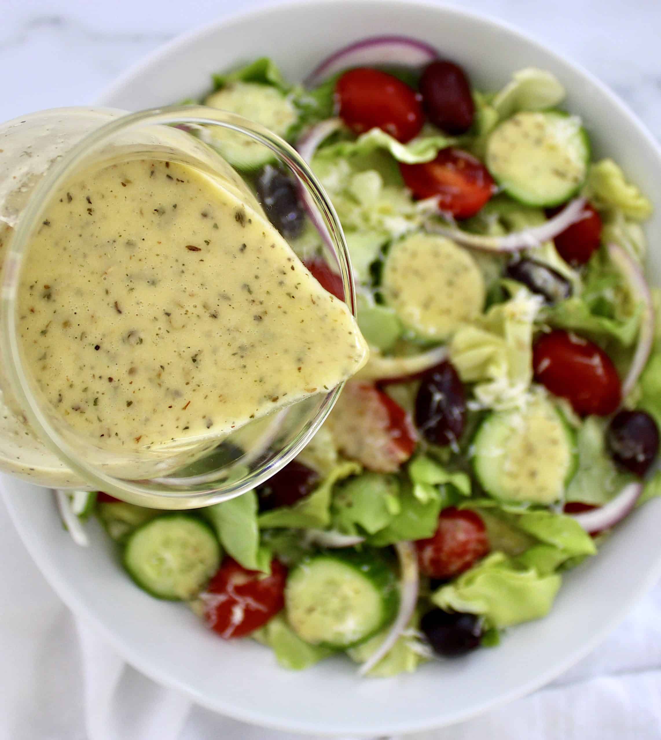 Homemade Italian Dressing being poured over salad in white bowl