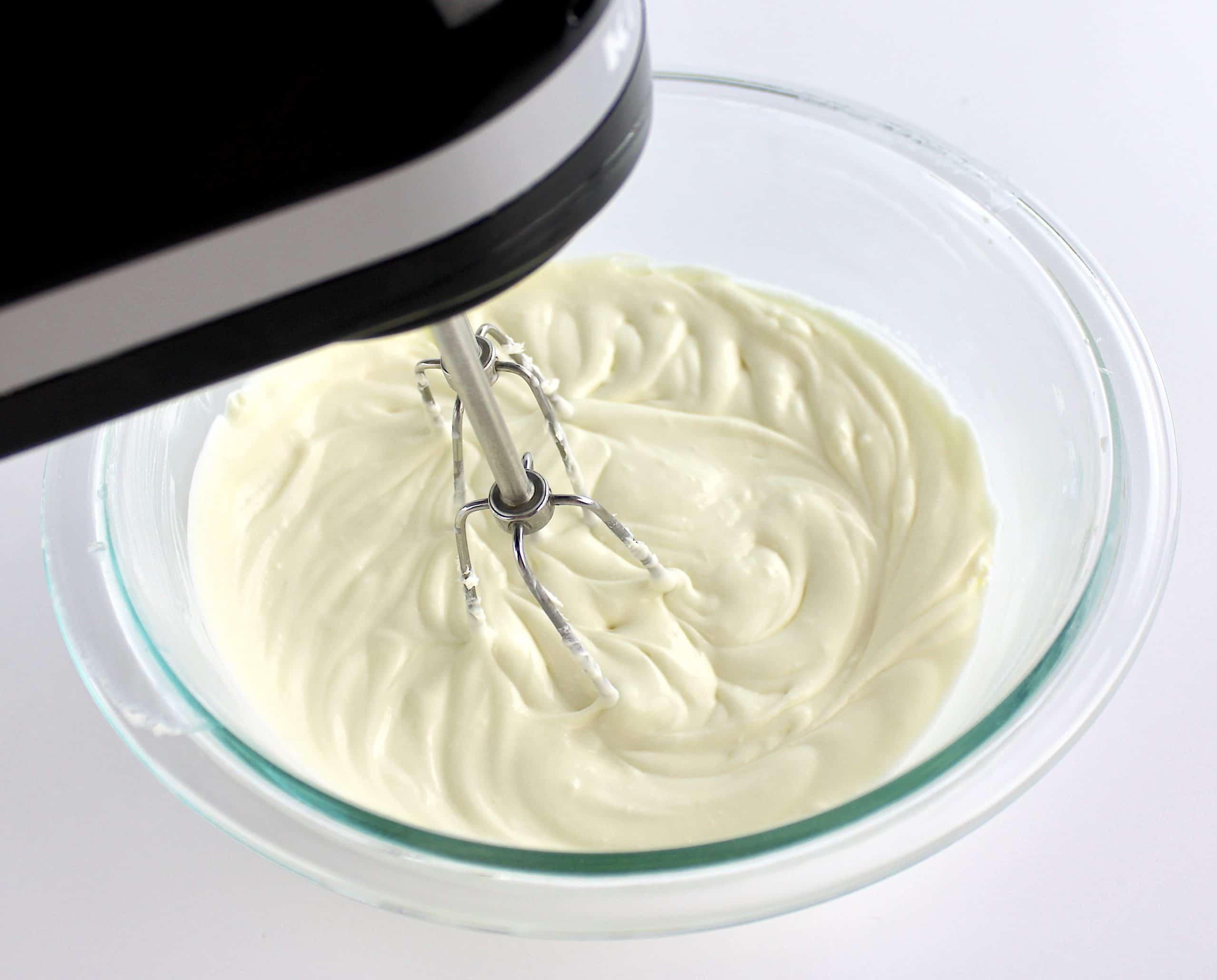 cheesecake batter in glass bowl being mixed with hand mixer