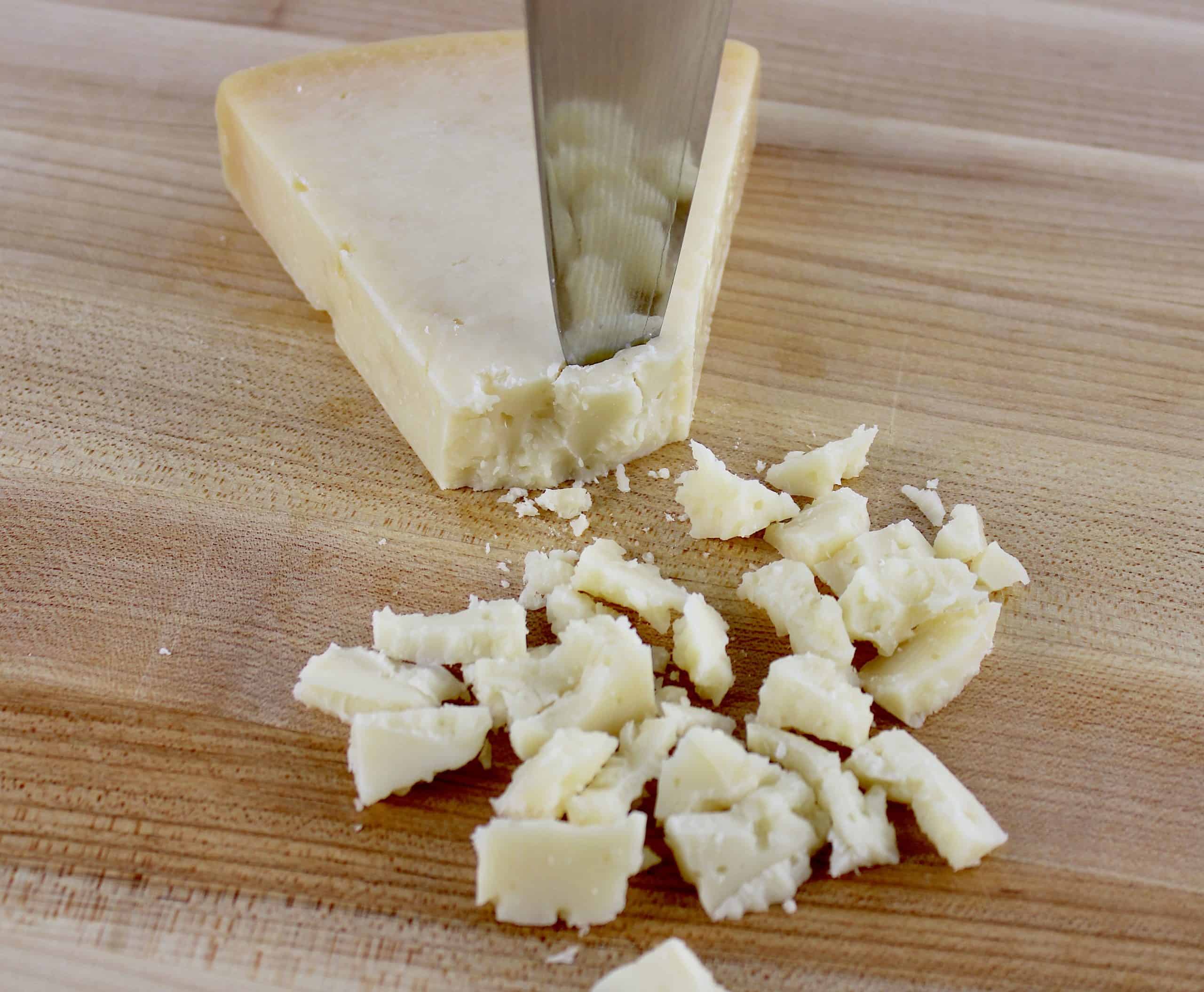 wedge of parmesan cheese with knife making chards