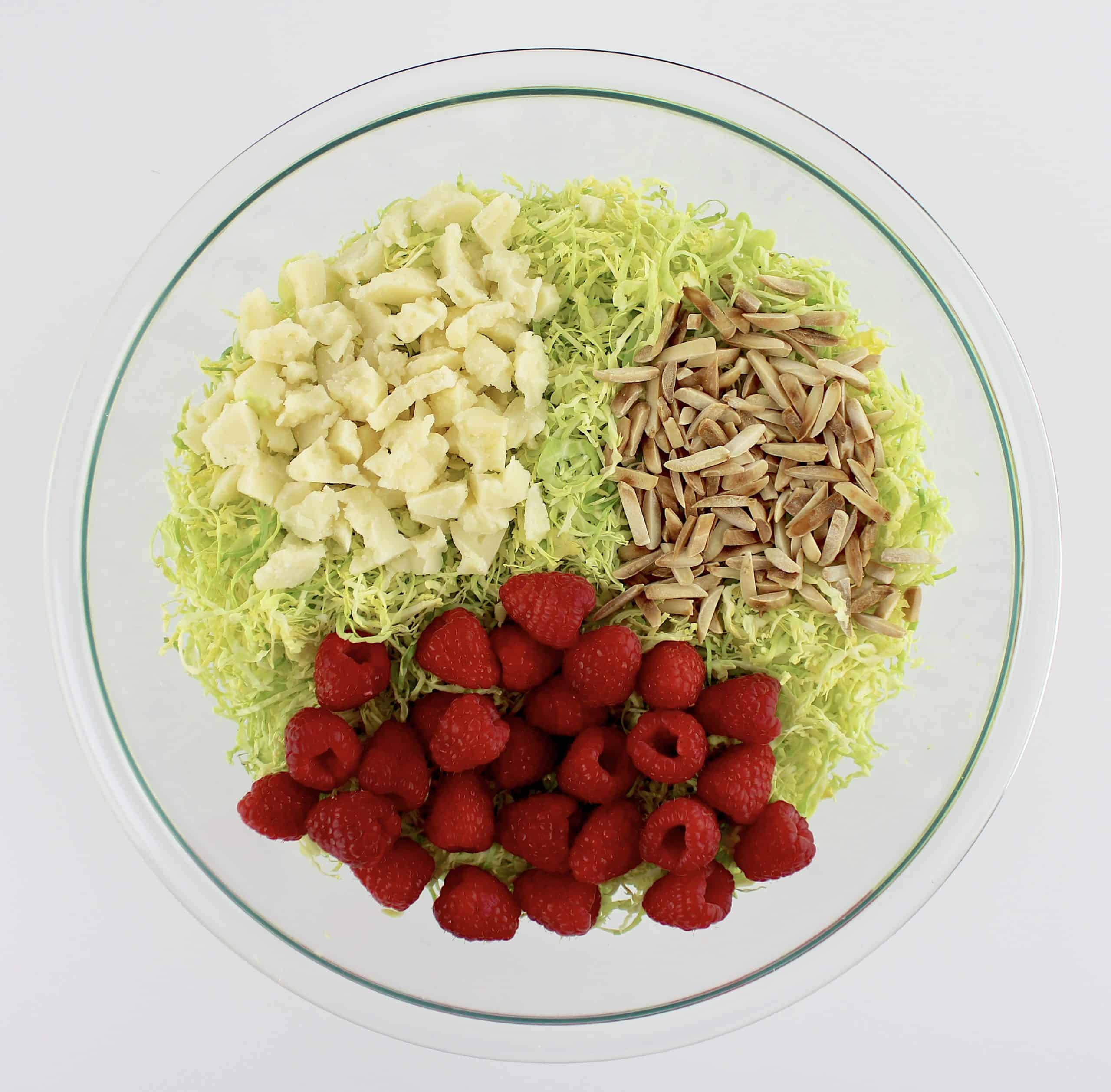 shaved brussels sprouts slivered toasted almonds raspberries and parmesan cheese shards in glass bowl