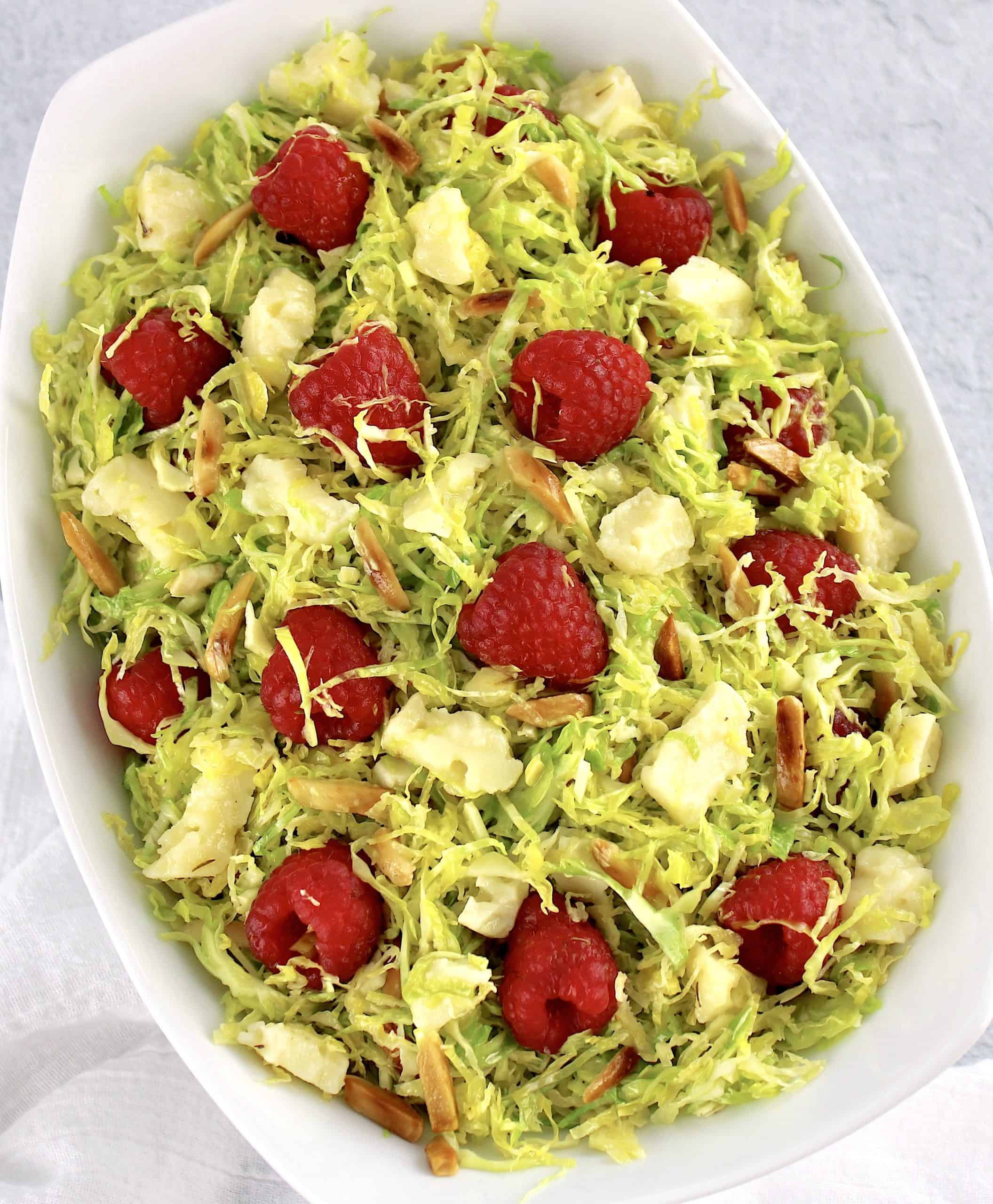 Shaved Brussels Sprouts Salad in white bowl with raspberries