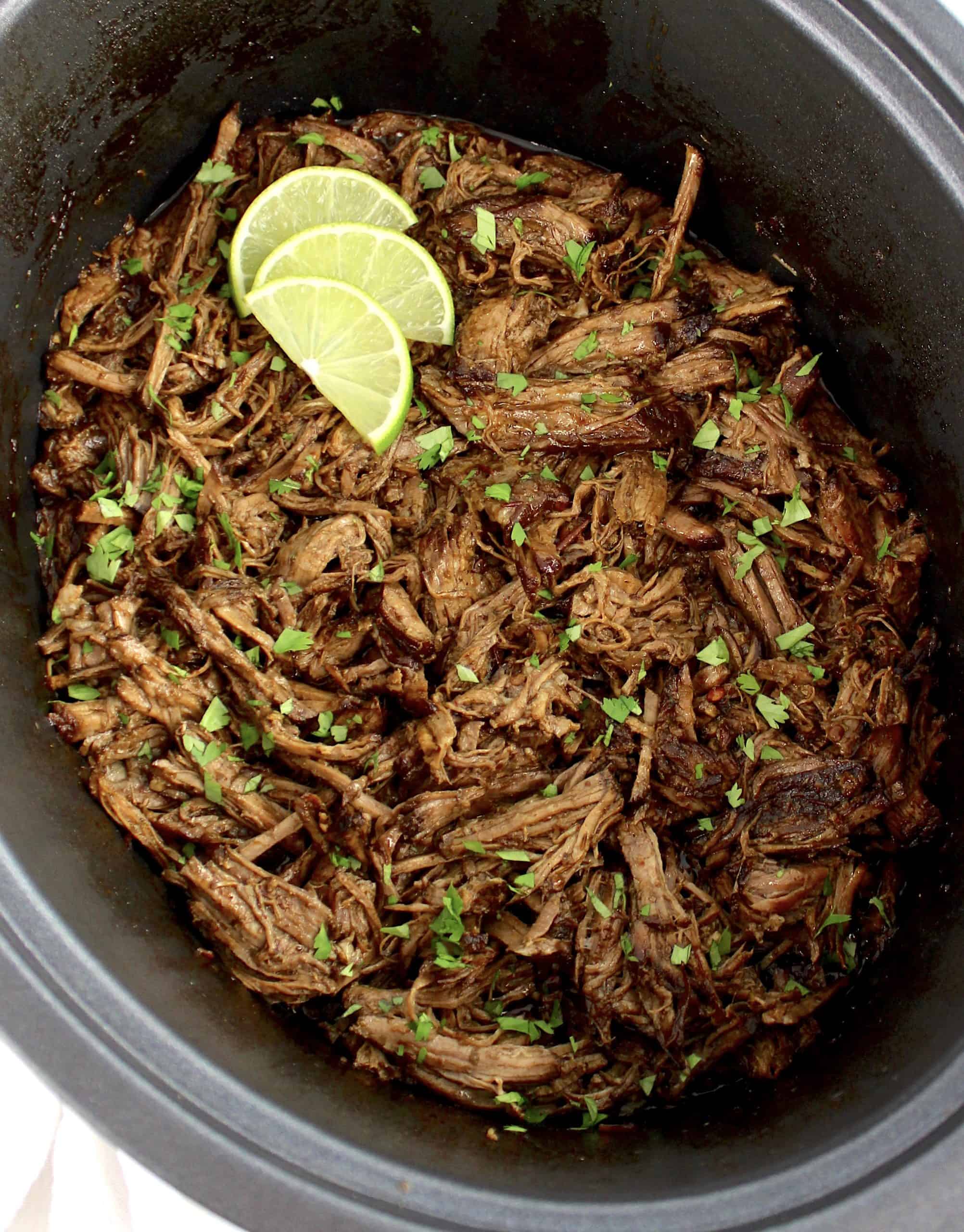 Beef Barbacoa with cilantro and lime slices in slow cooker