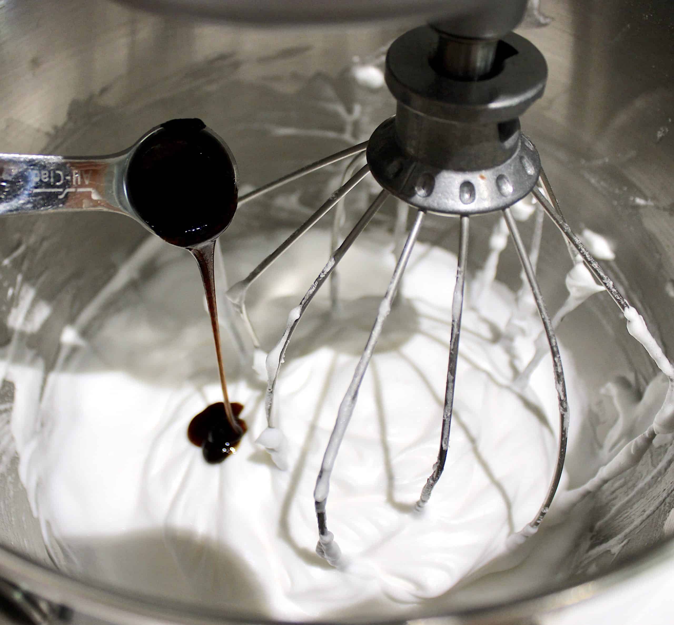 vanilla bean paste being poured into whipped egg whites in stand mixer
