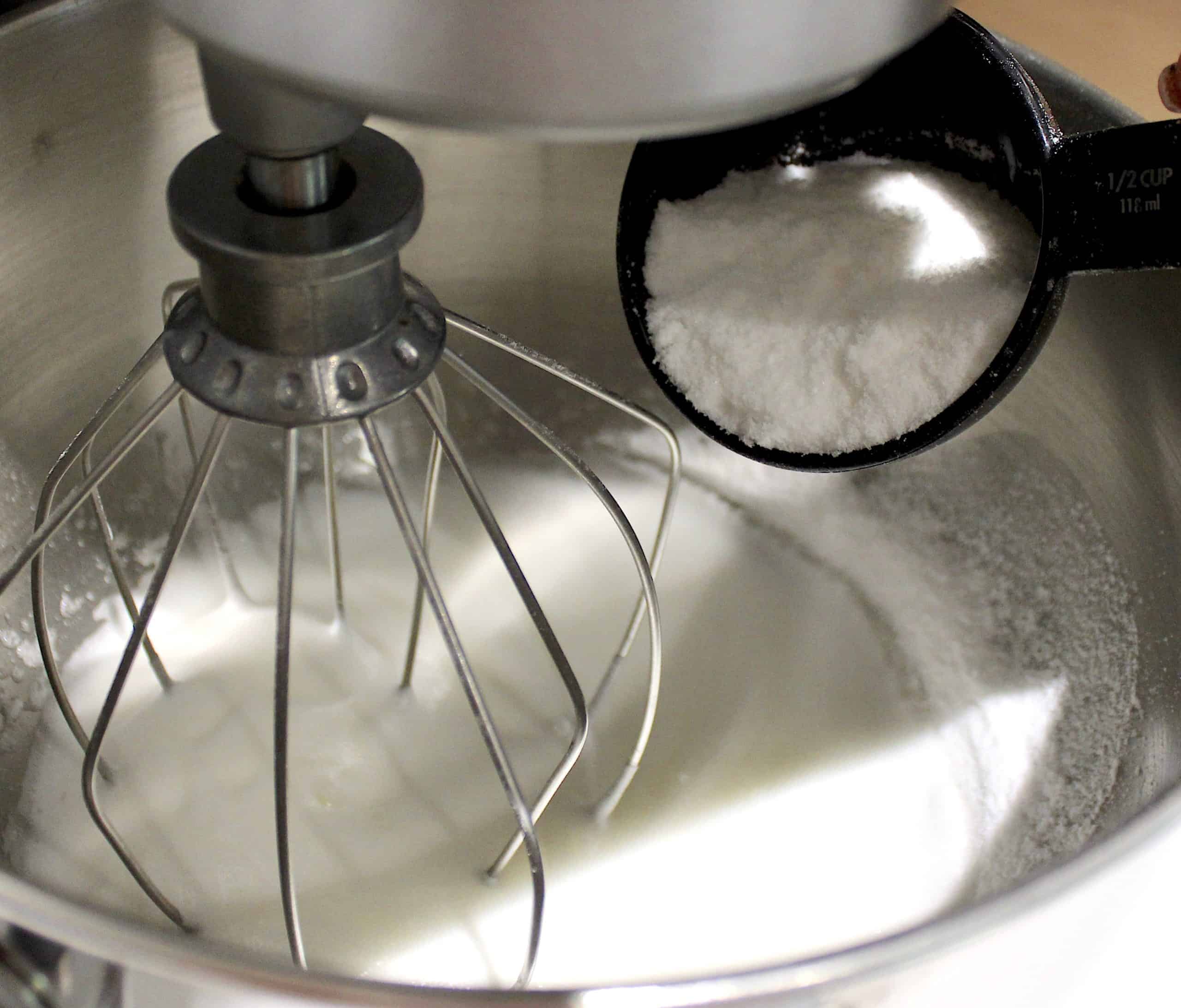 egg whites being whipped in stand mixer with sweetener being poured in