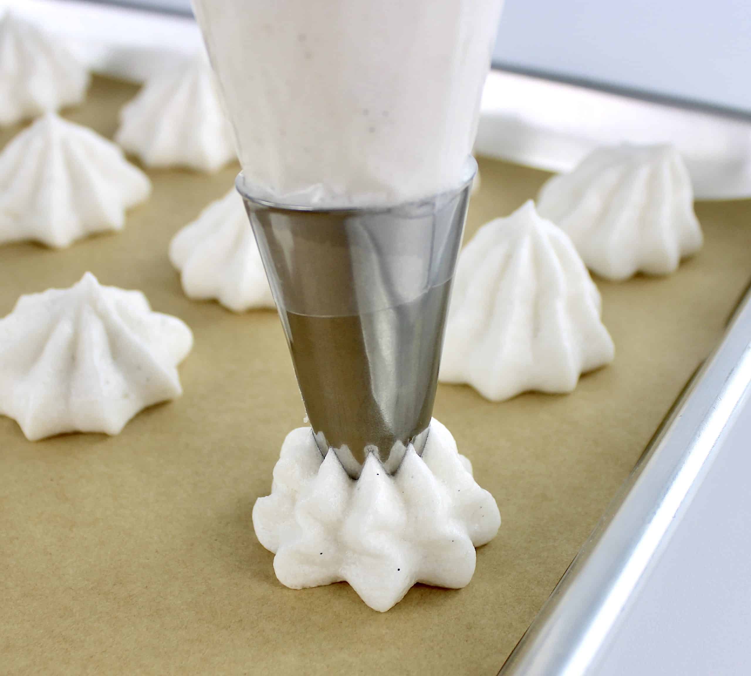 meringues being piped out onto parchment lined baking sheet