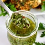 chimichurri sauce being spooned out of glass jar with chicken in background