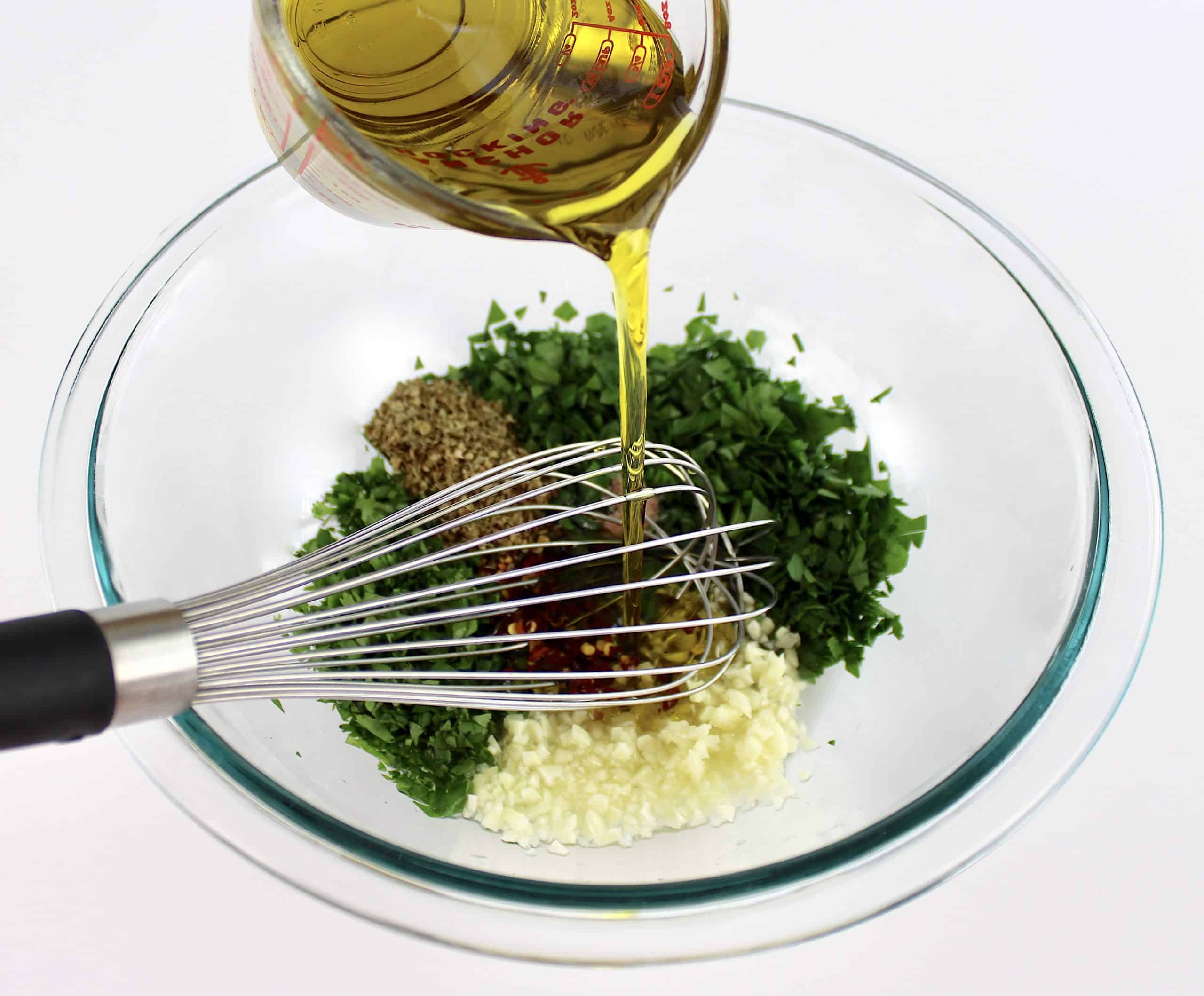Chimichurri Sauce ingredients unmixed with olive oil being whisked in