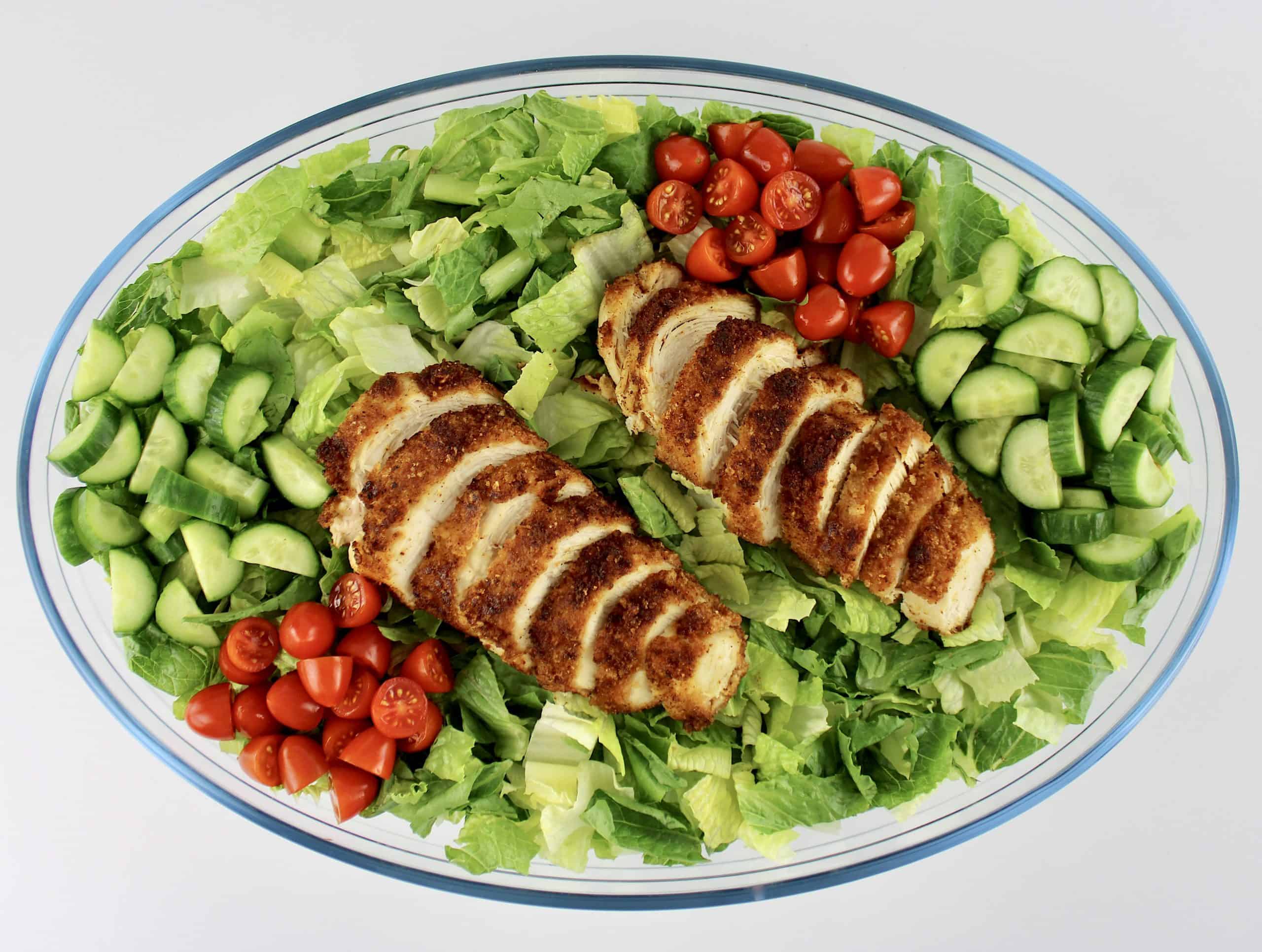 lettuce sliced chicken chopped tomatoes and cucumbers in oval glass bowl