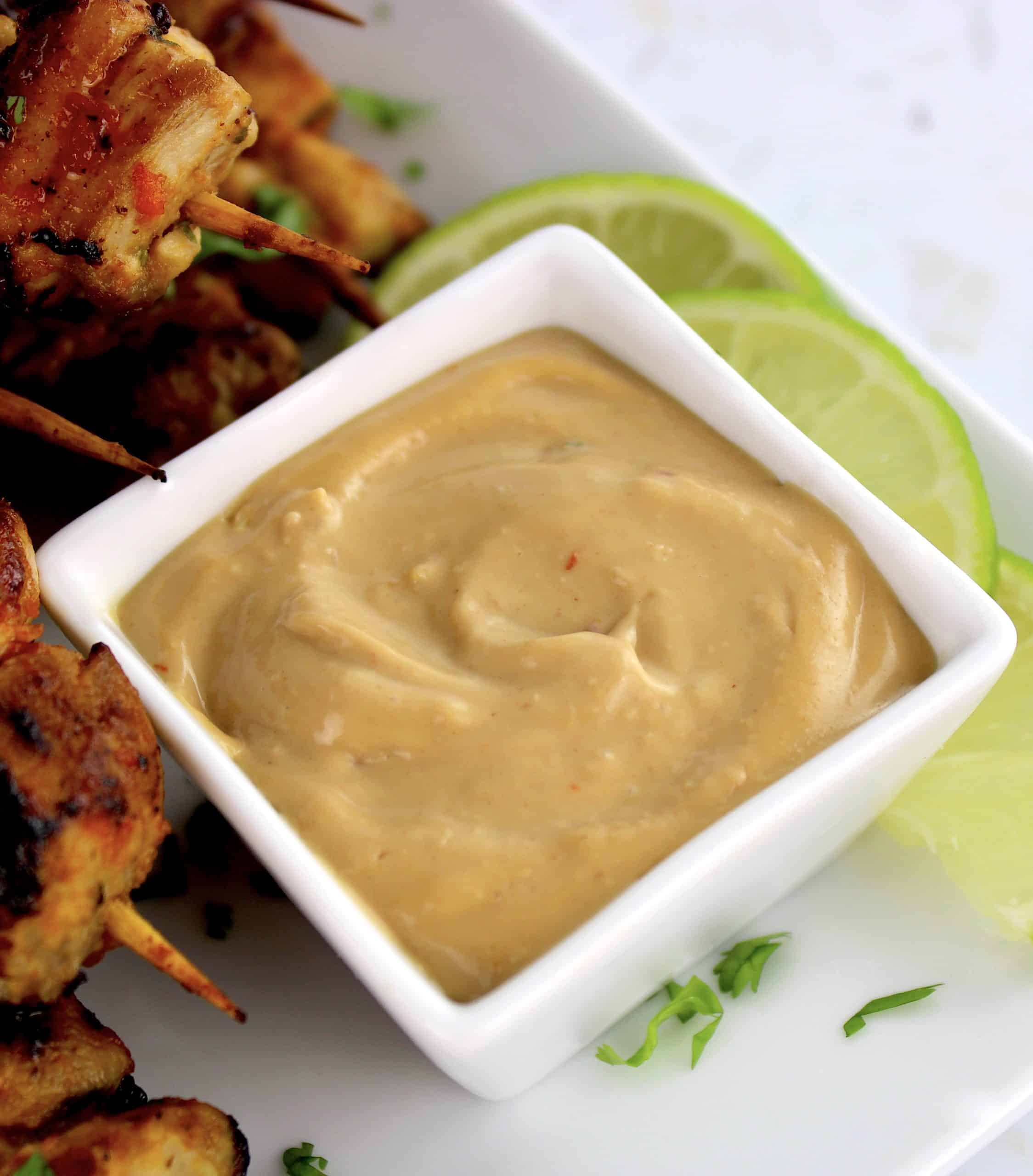 Easy Peanut Sauce in white square bowl with satay in background