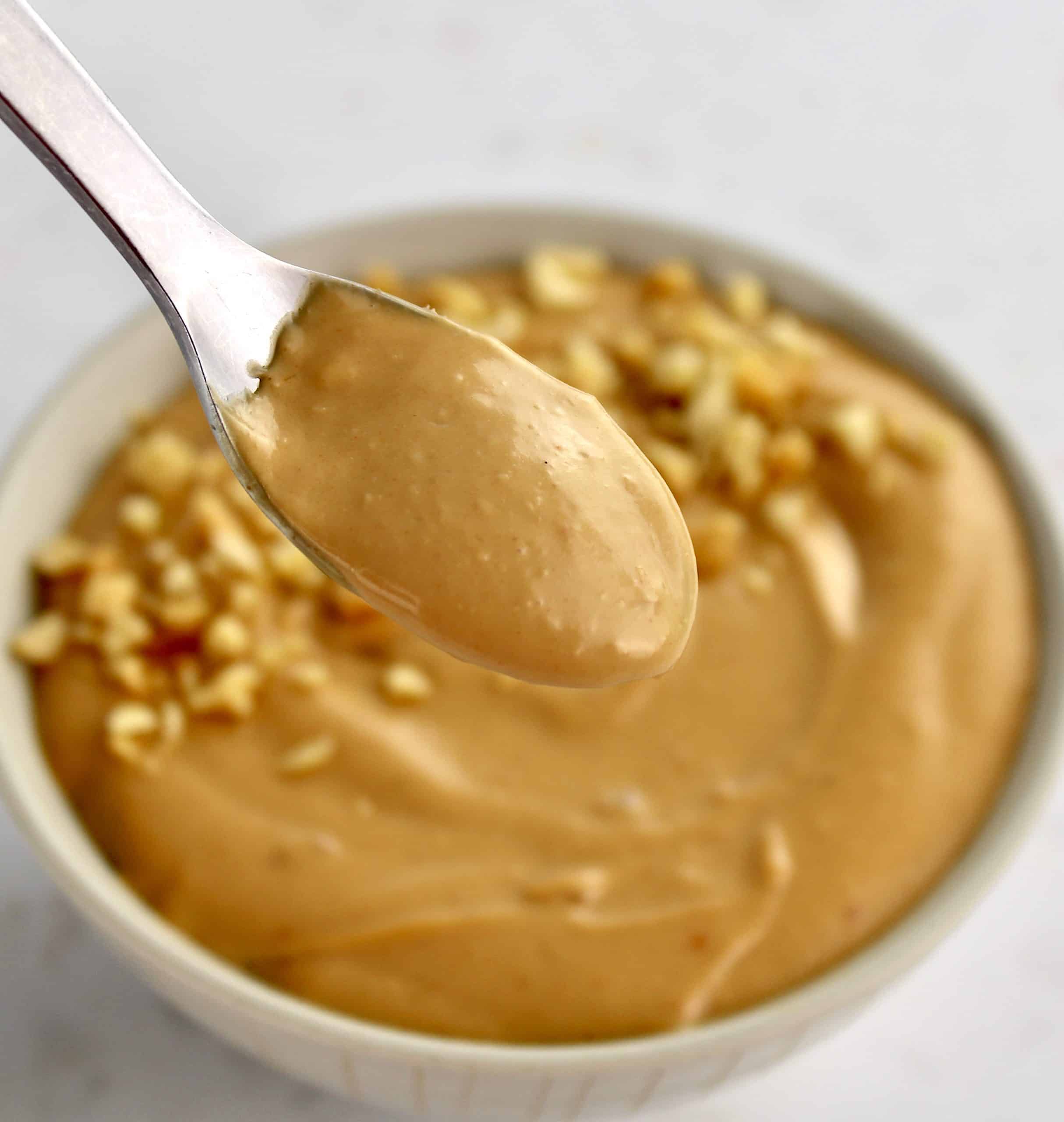 peanut sauce in spoon held up over more in beige bowl in background