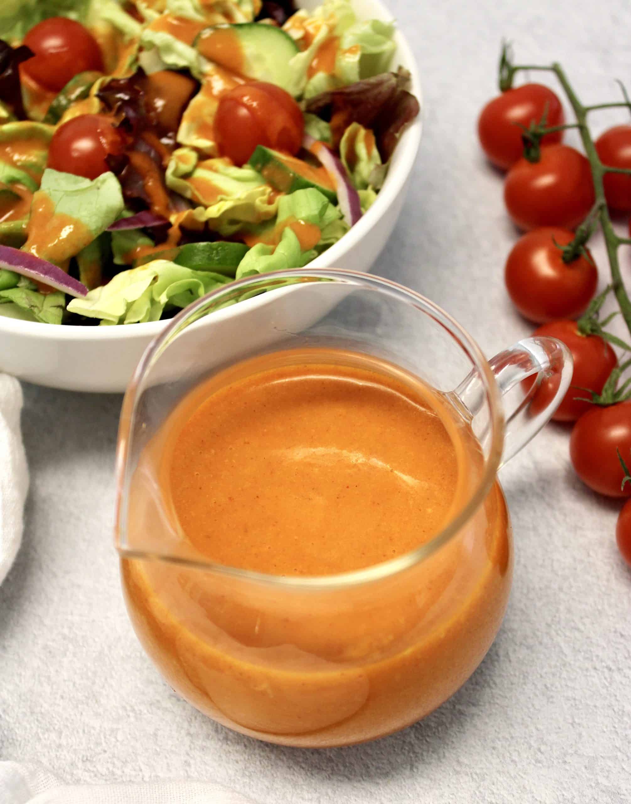 Keto Catalina Dressing in glass container with salad and tomatoes in background