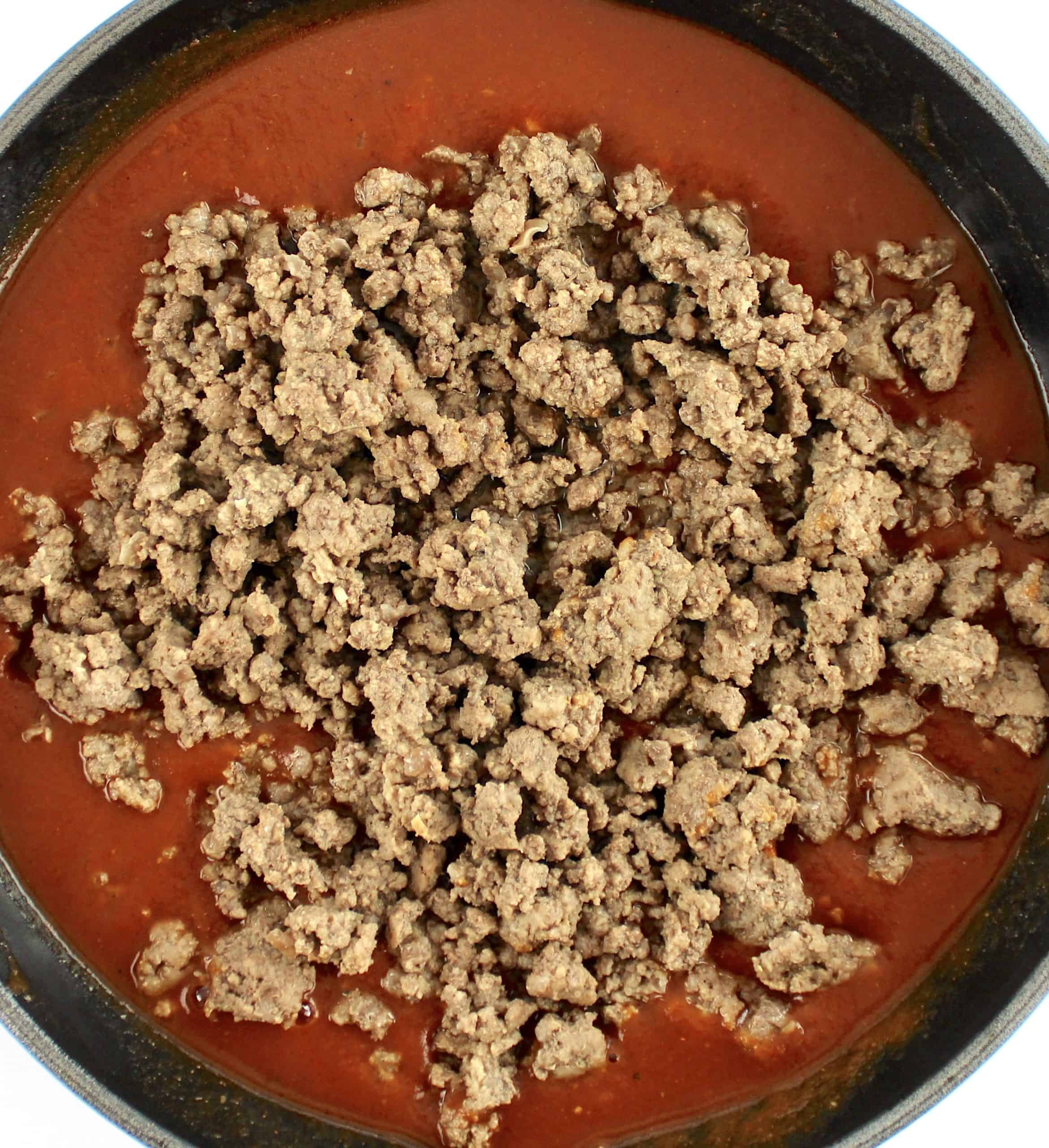 sloppy joe sauce in skillet with cooked ground beef on top unmixed