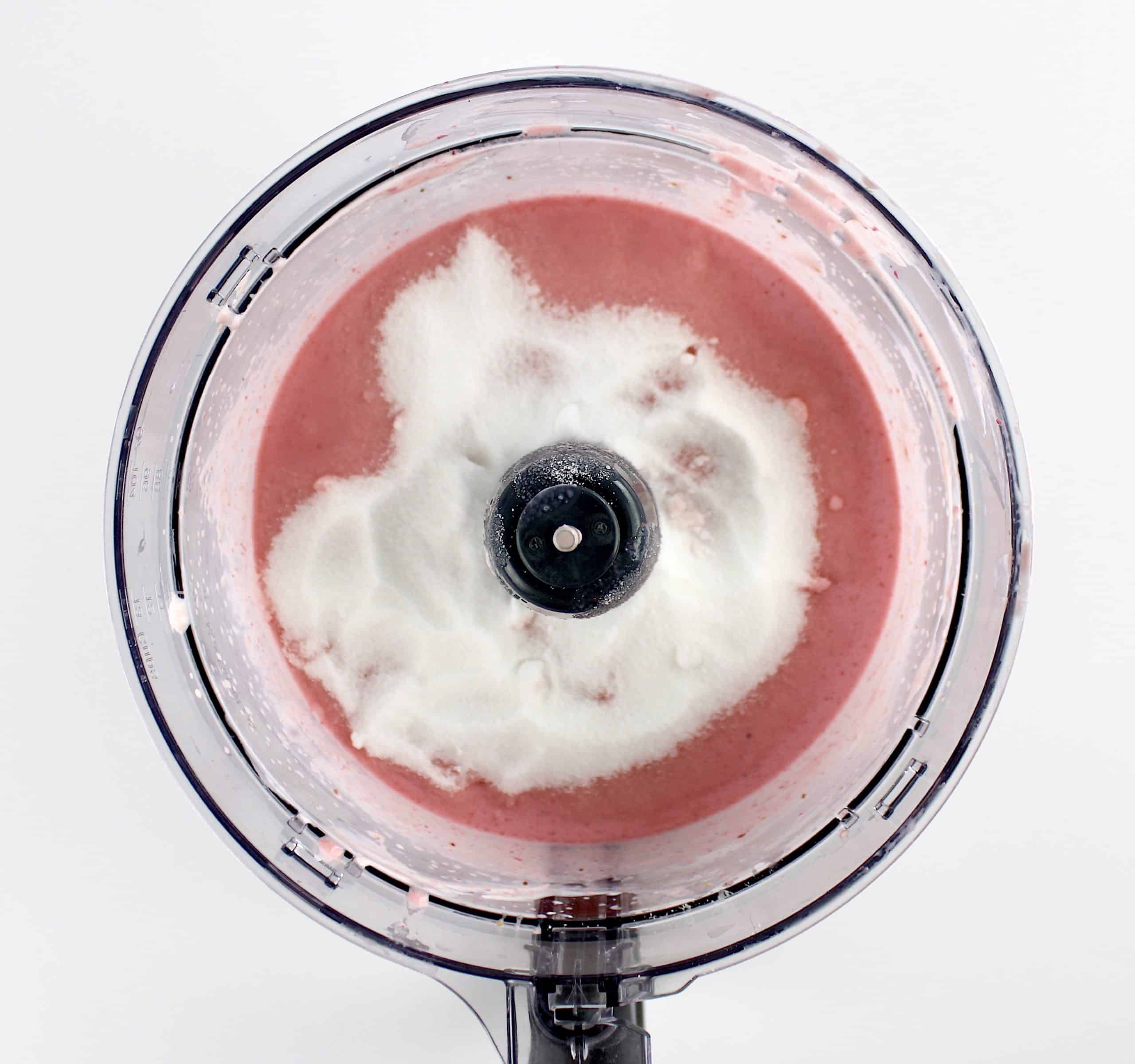 Keto Strawberry Frozen Yogurt mixture with sweetener on top in food processor