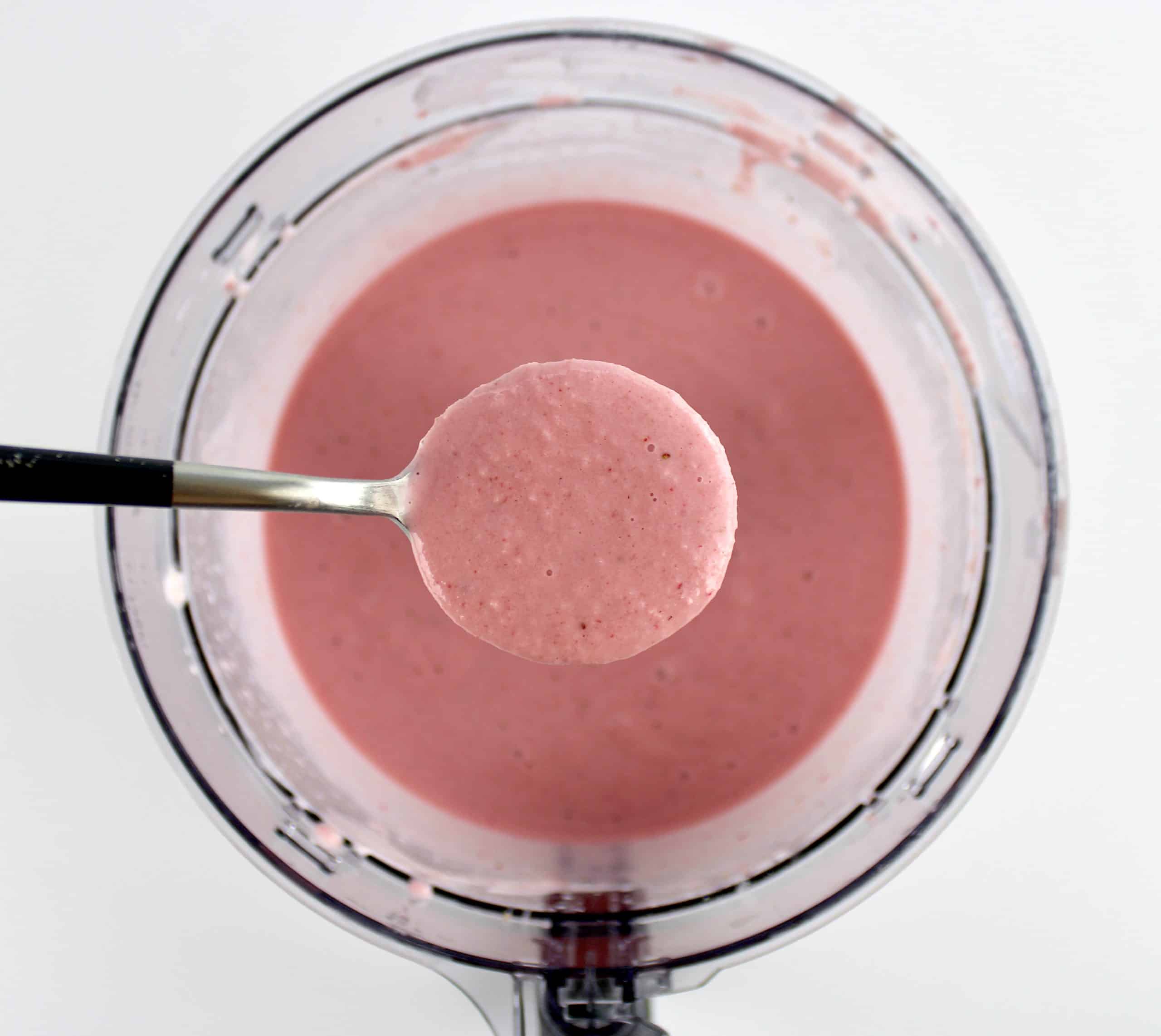 Keto Strawberry Frozen Yogurt mixture in spoon held over food processor