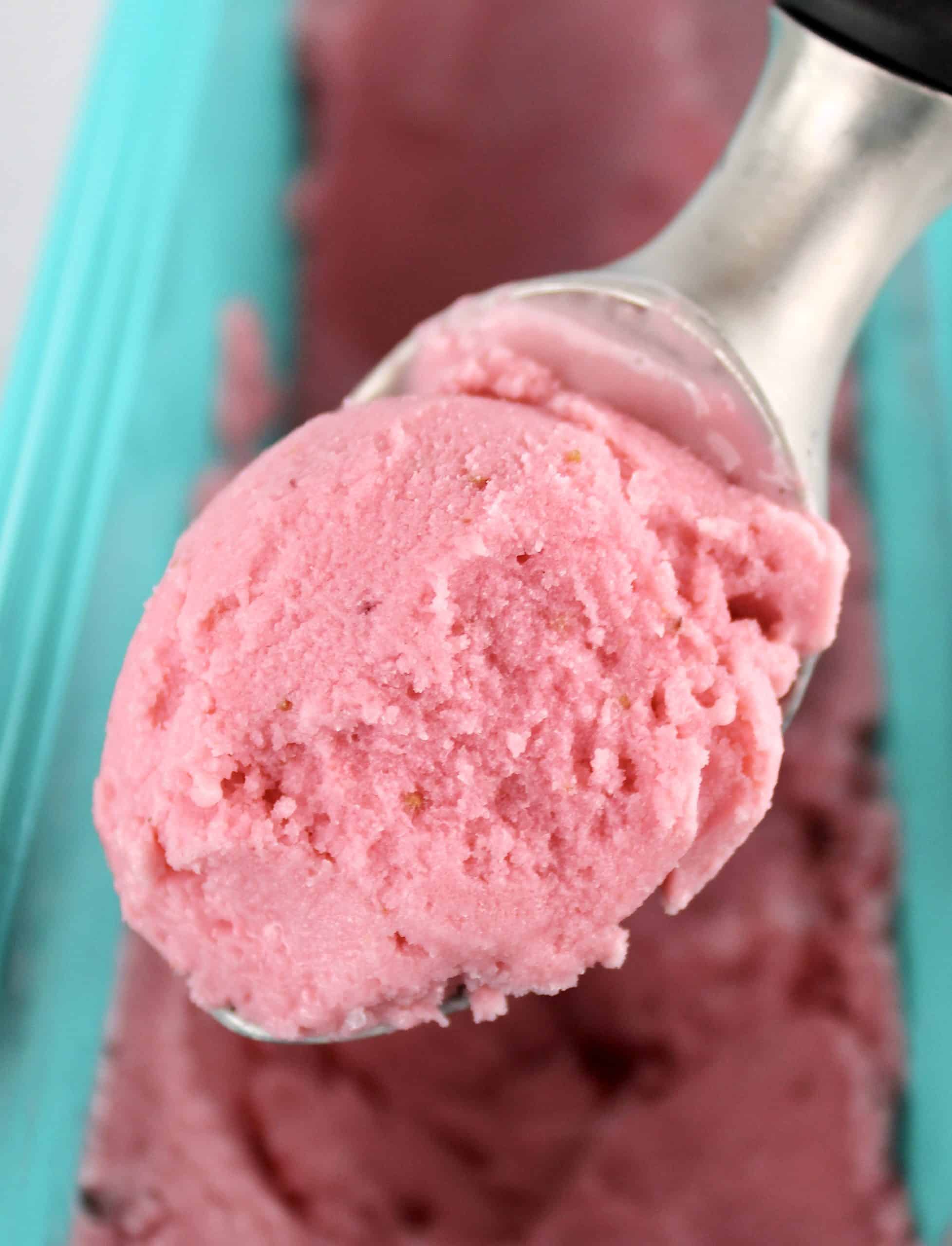 scoop of Keto Strawberry Frozen Yogurt held up over a teal container