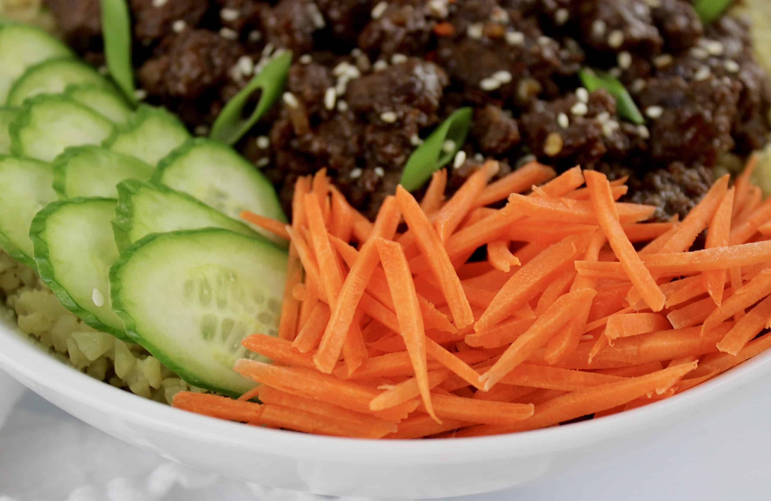 Korean Beef Bowl with shredded carrots and sliced cucumbers closeup