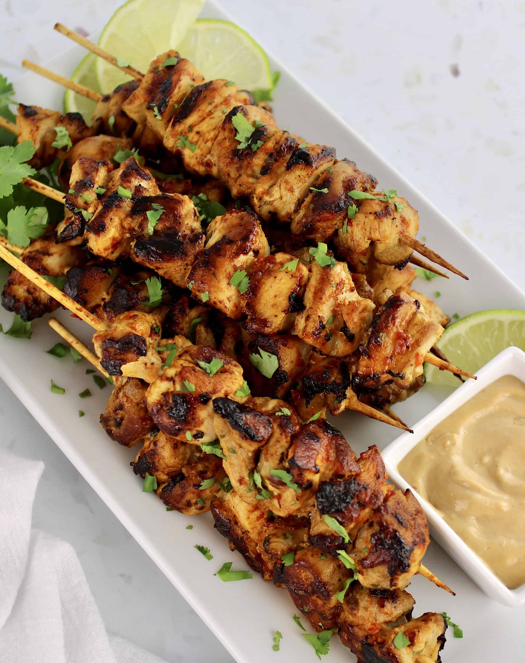 Thai Chicken Satay skewers on white plate with peanut sauce on side