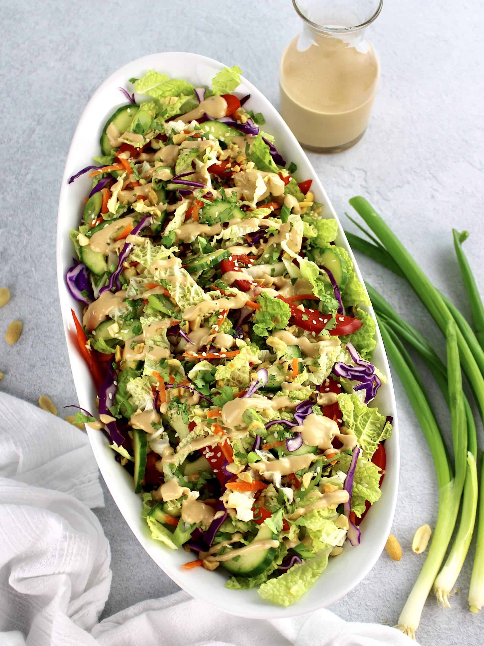 Thai Crunch Salad with Peanut Dressing in white bowl with scallions and dressing in background