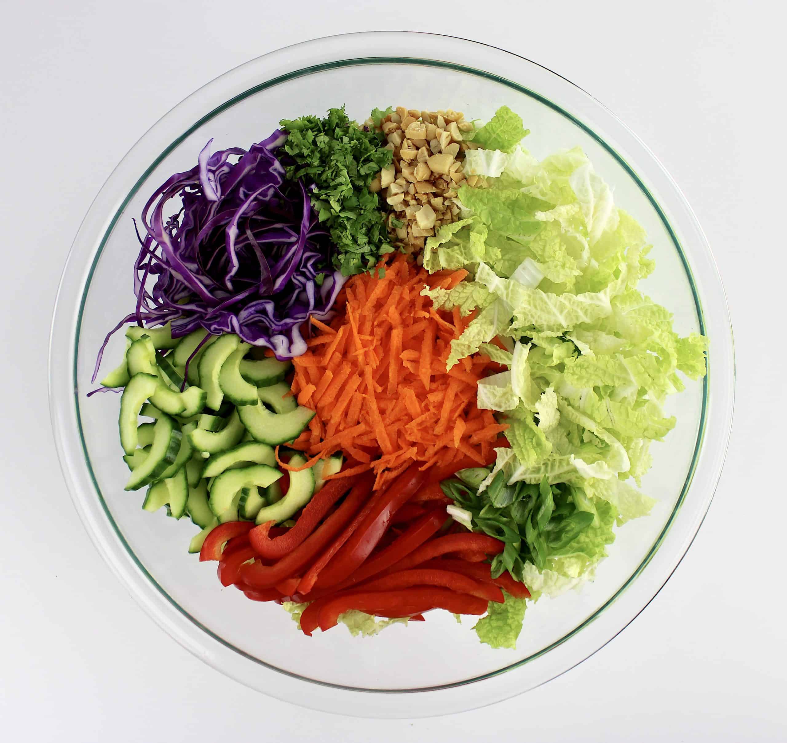 cabbage red bell pepper cucumbers peanuts scallions and carrots all shredded in glass bowl