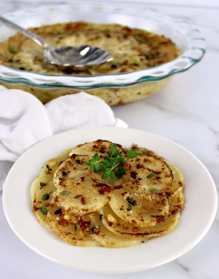 Turnips Au Gratin in round white dish with glass casserole in background