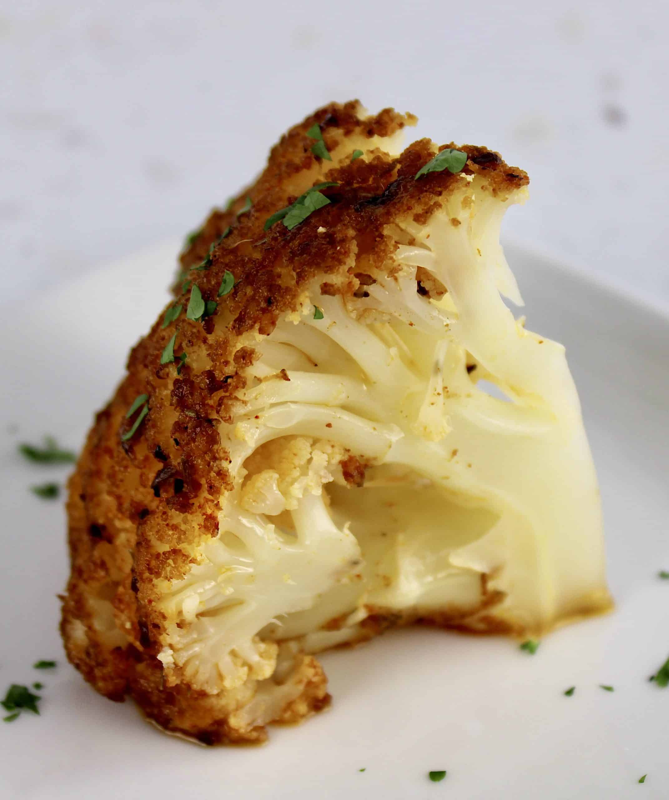 wedge of Whole Roasted Cauliflower on white plate with parsley
