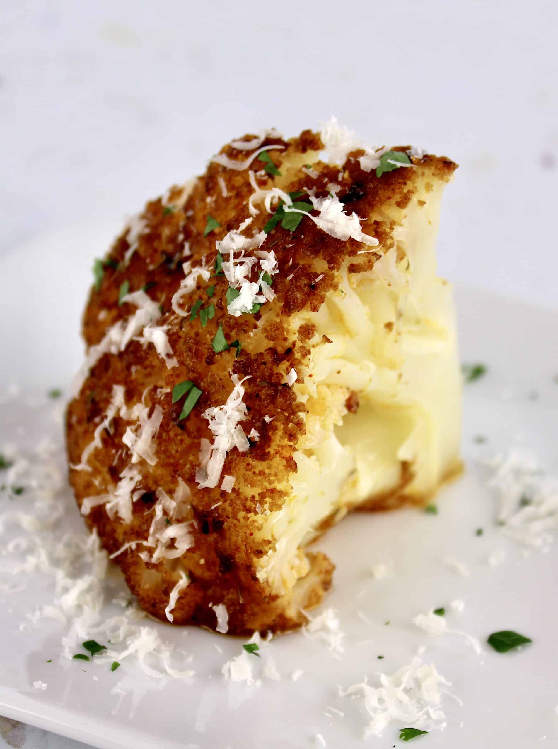 wedge of Whole Roasted Cauliflower on white plate with grated parmesan