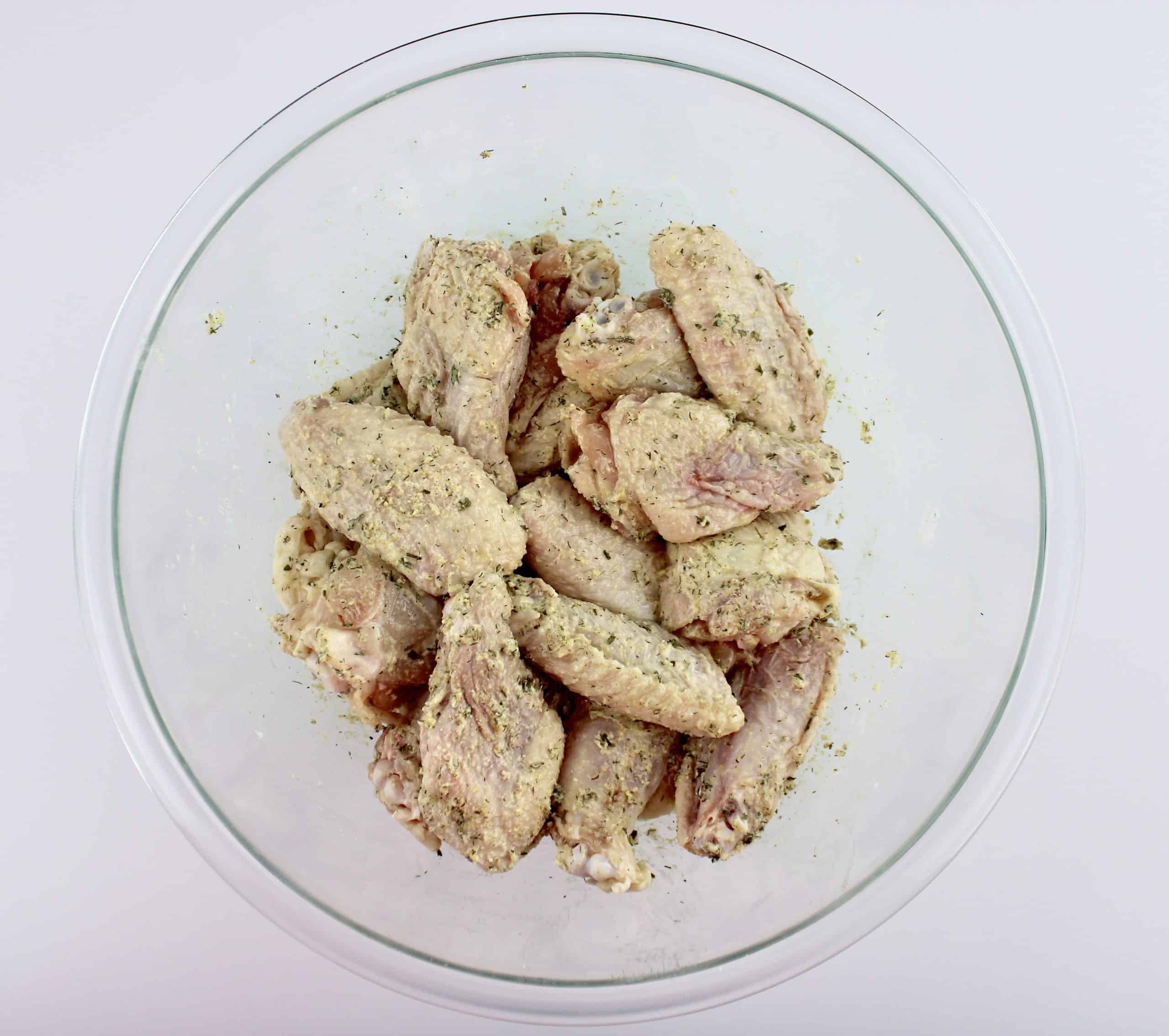 raw chicken wings tossed with ranch seasoning in glass bowl