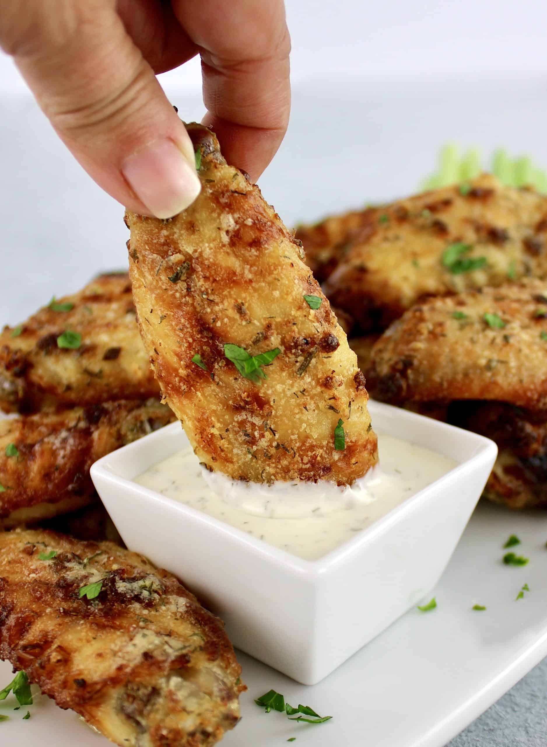 ranch chicken wing being dipped into ranch dressing in square white bowl with more wings in background