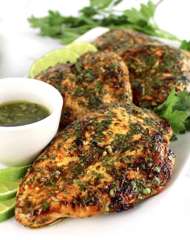 Chicken Chimichurri on white plate with sauce in white bowl on side and lime slices