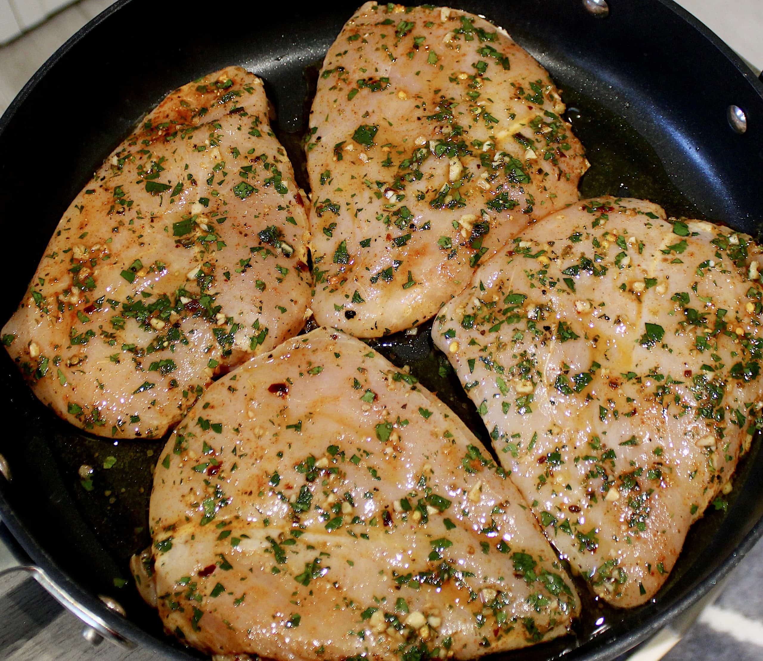 4 raw Chimichurri marinated chicken breasts in skillet