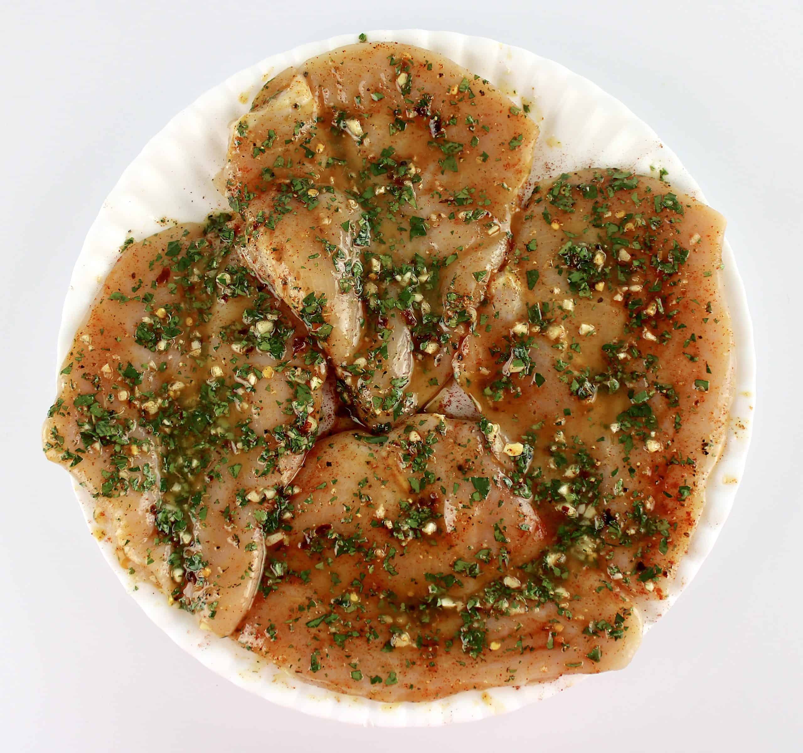 4 raw chicken breasts on white plate marinating in Chicken Chimichurri sauce