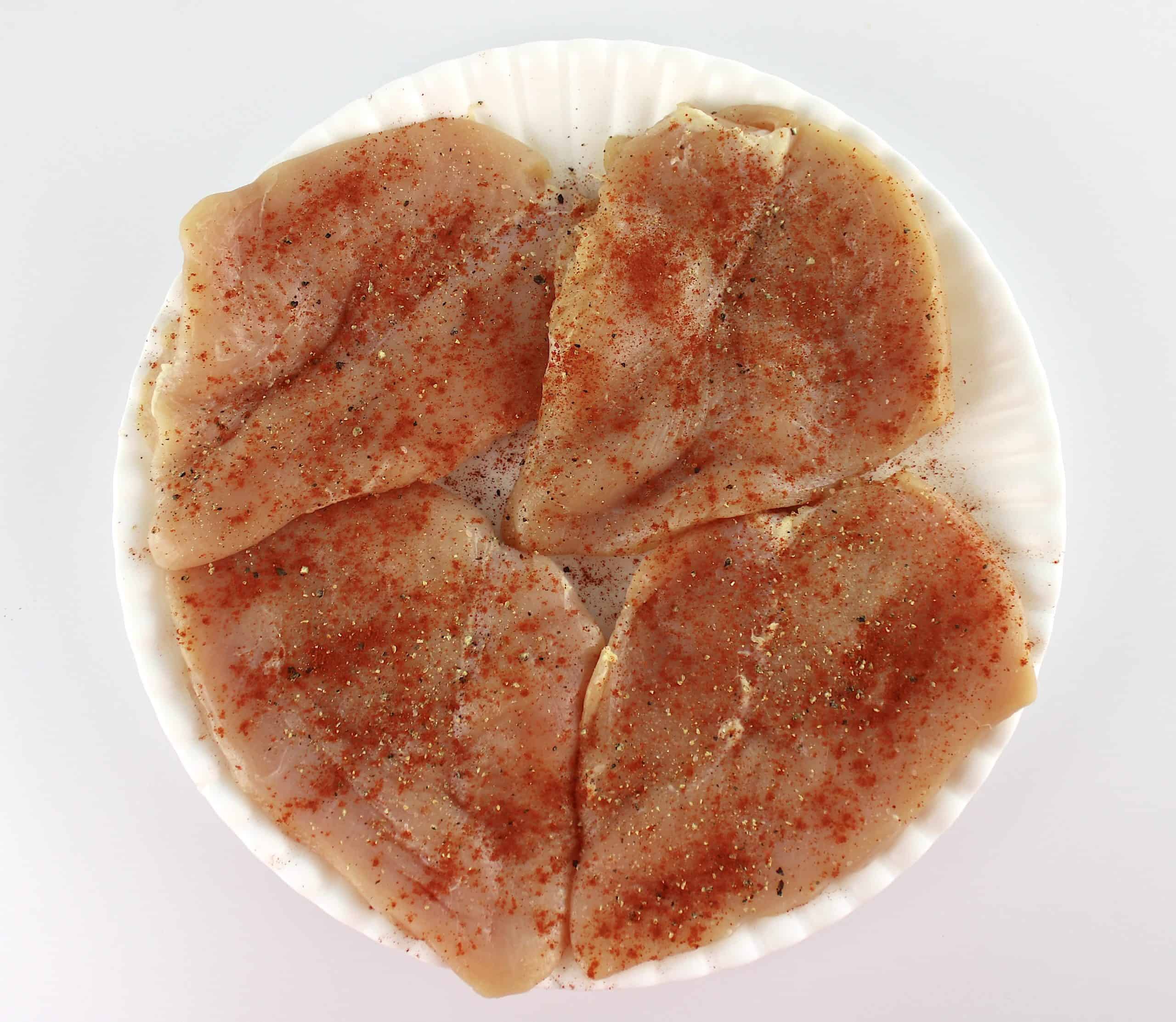 4 raw chicken breasts on white plate with salt pepper and smoked paprika