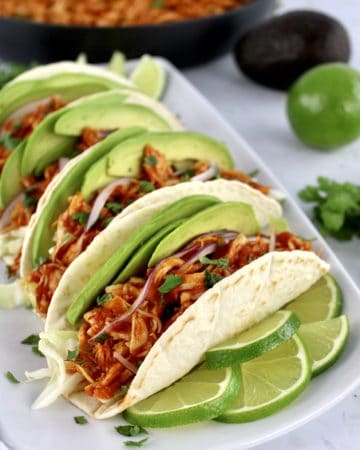 closeup of Chicken Tinga in tortillas on white plate with limes slices on side