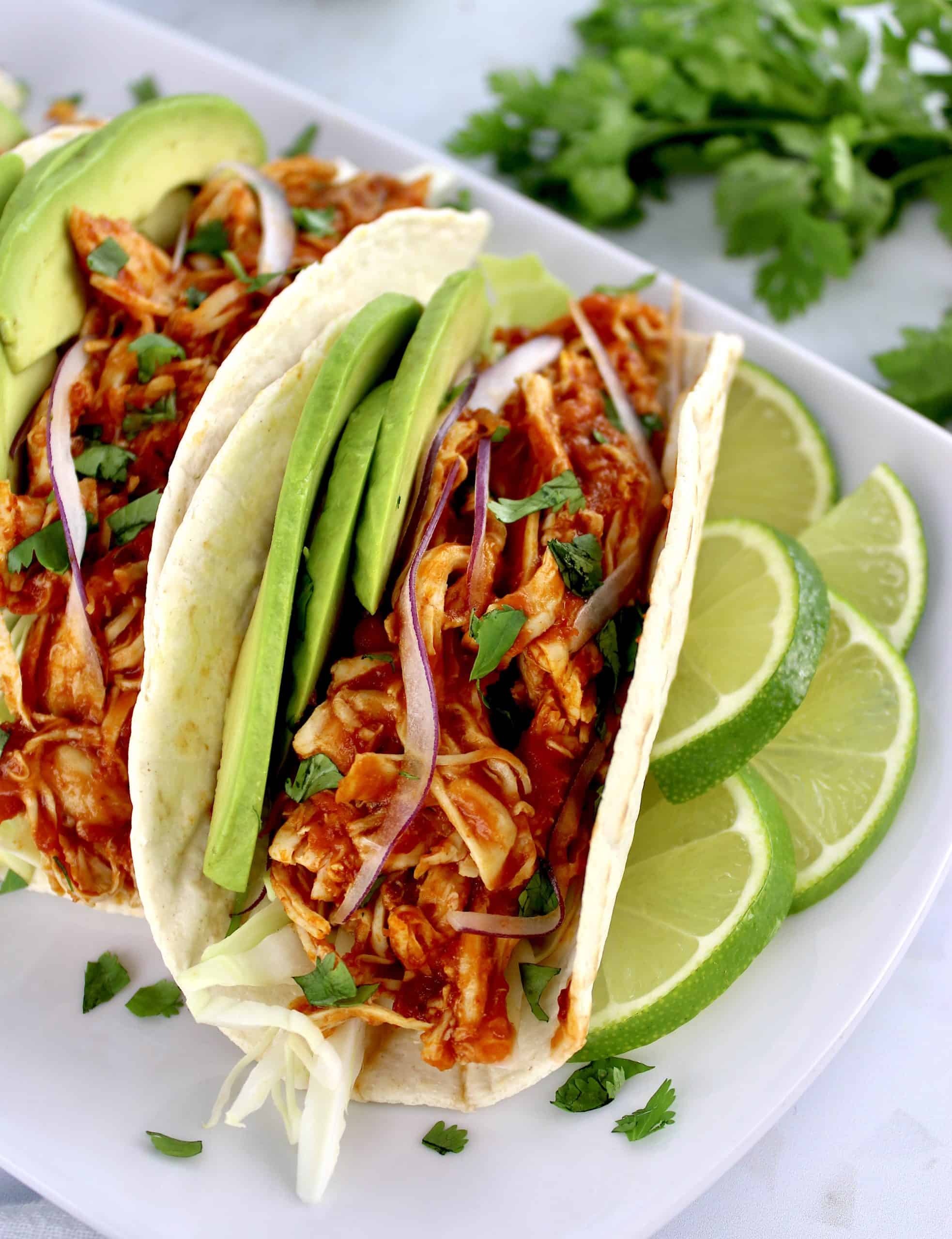closeup overhead view of Chicken Tinga in tortilla on white plate with lime slices on side