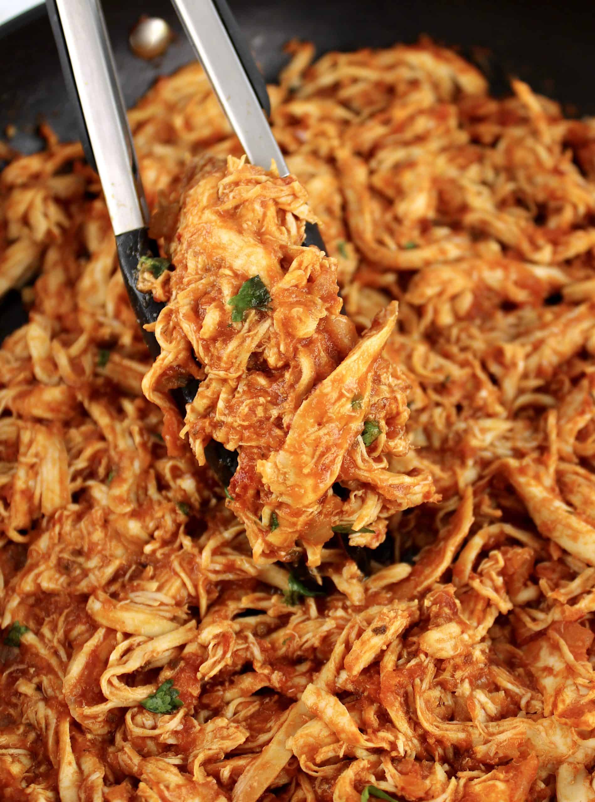 Chicken Tinga in skillet held up with tongs