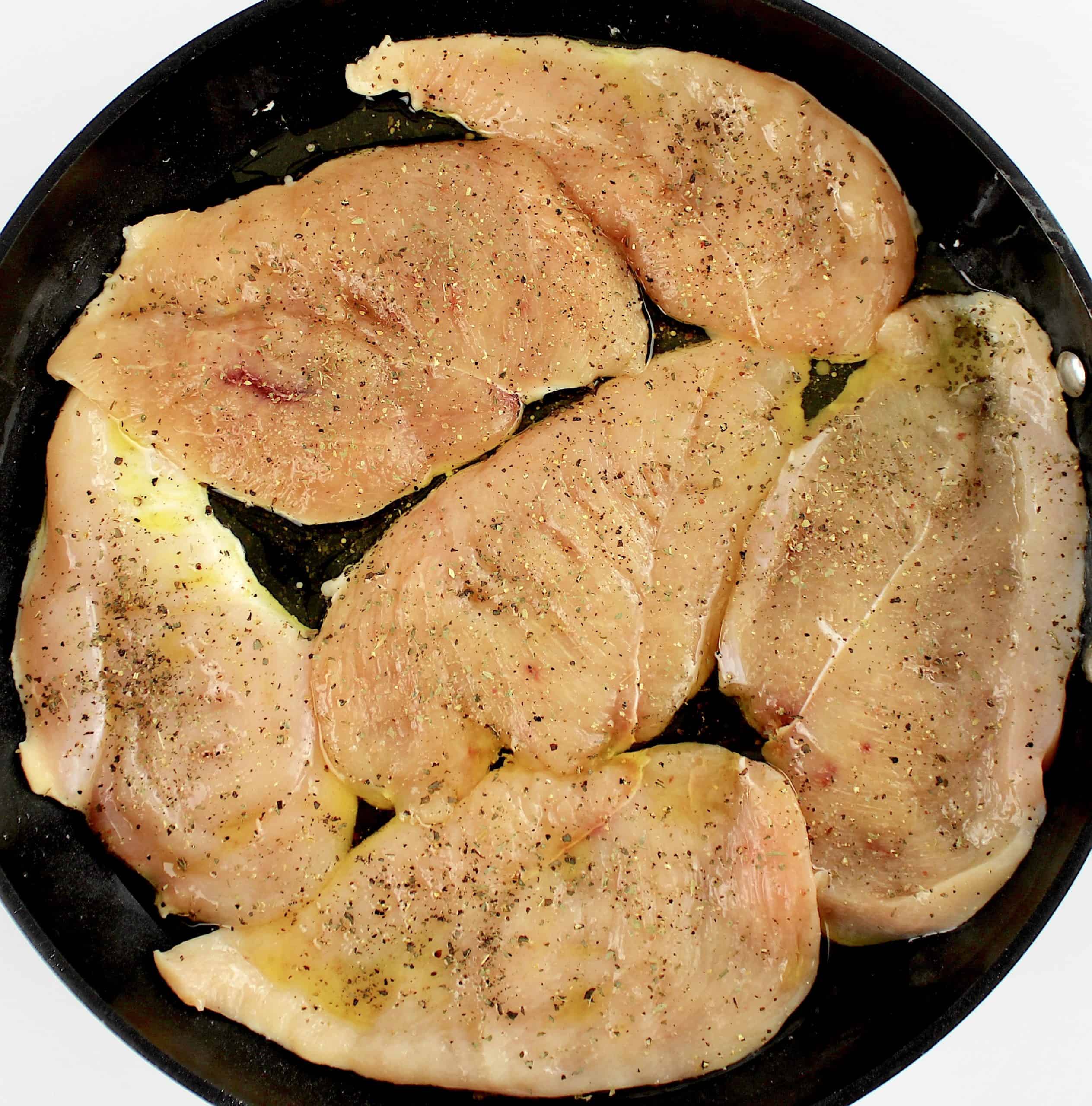 6 raw chicken breasts in skillet with salt pepper and basil