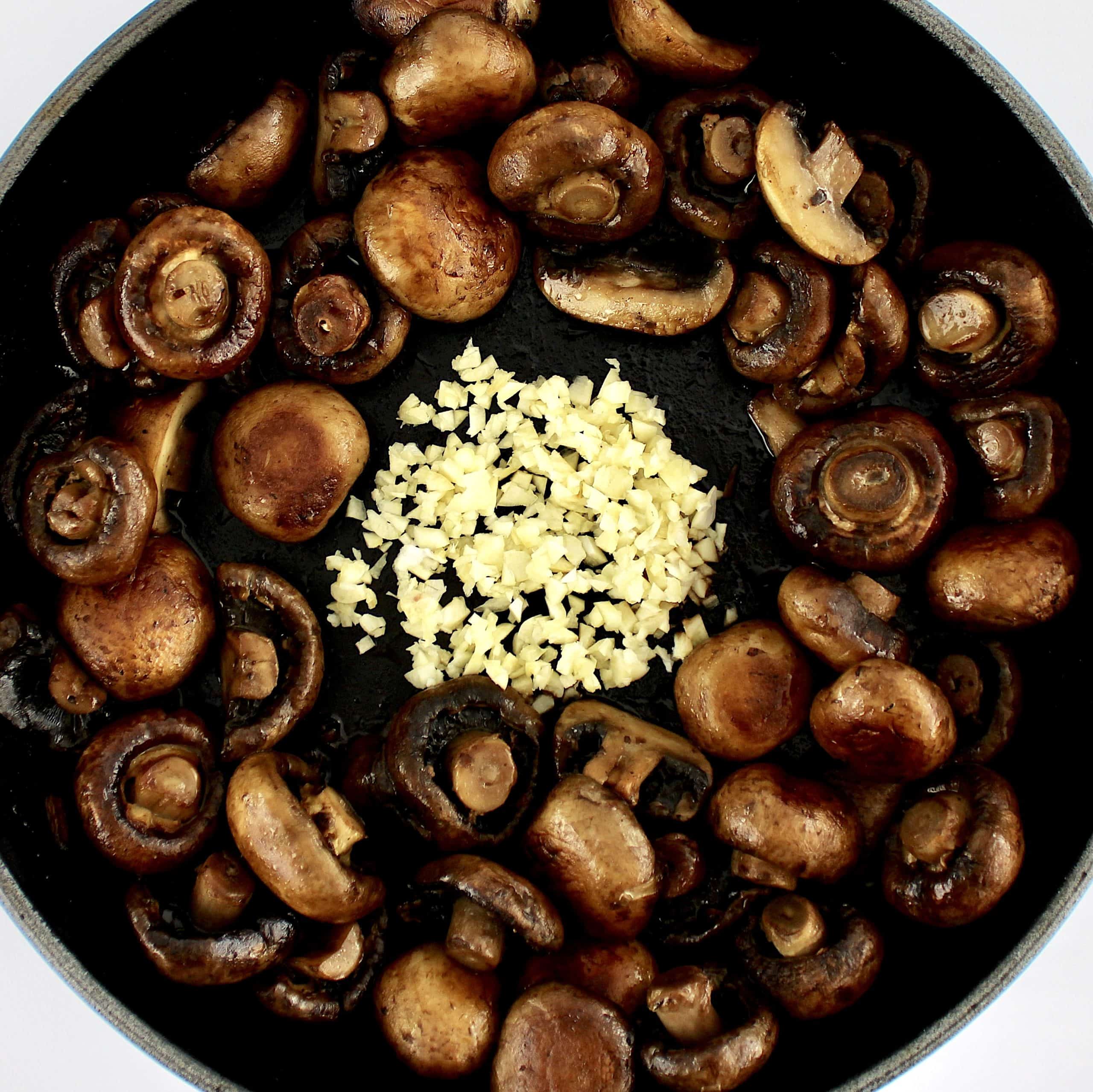 baby bella mushrooms sautéing in skillet with minced garlic in the center