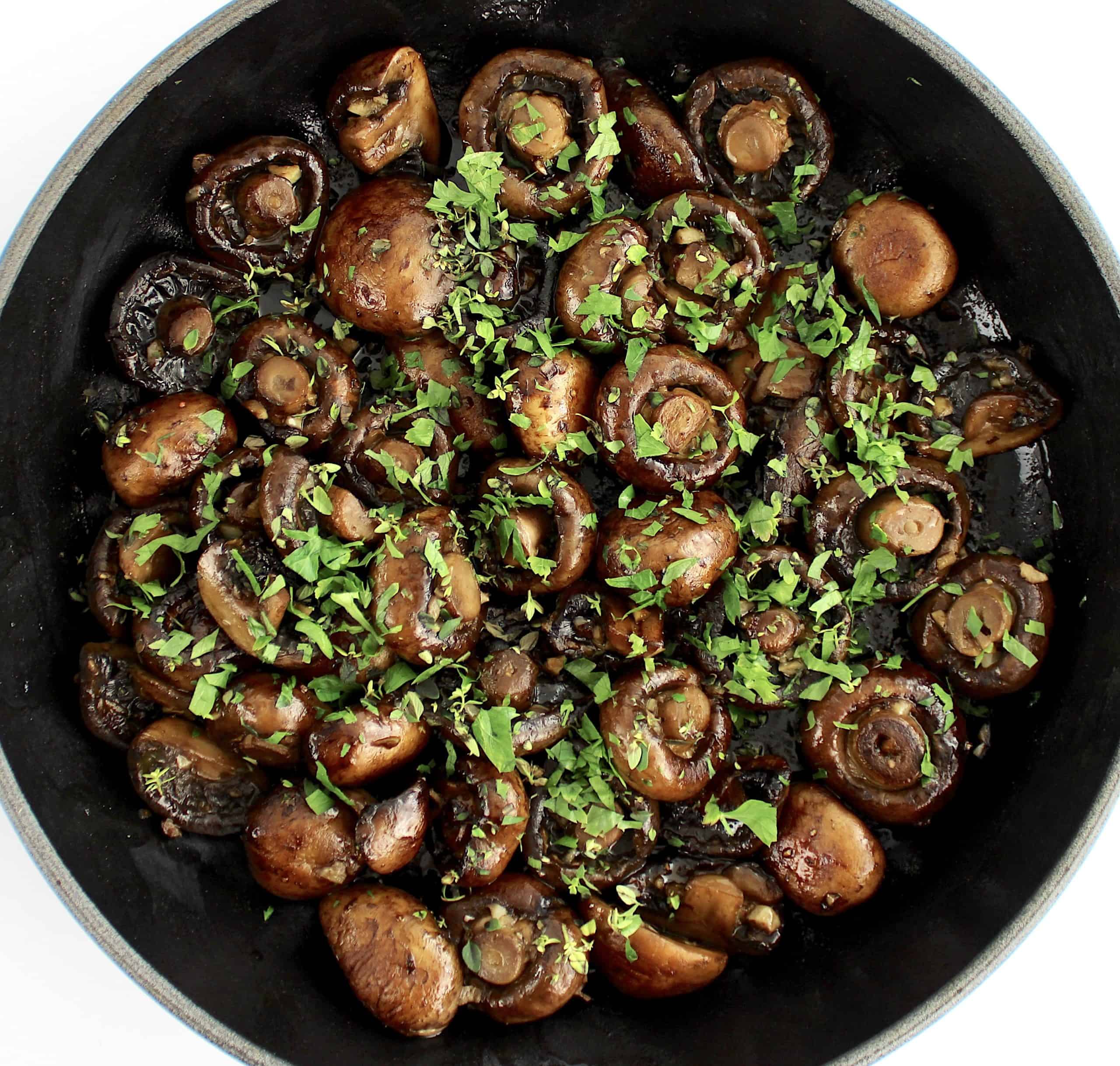 sauteed baby bella mushrooms in skillet with chopped herbs on top