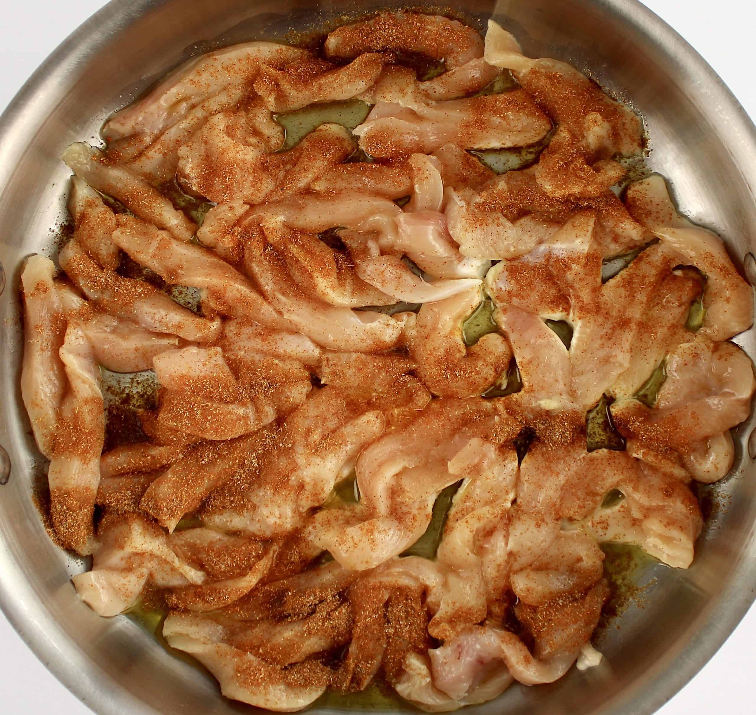 raw chicken strips in skillet with fajita seasoning