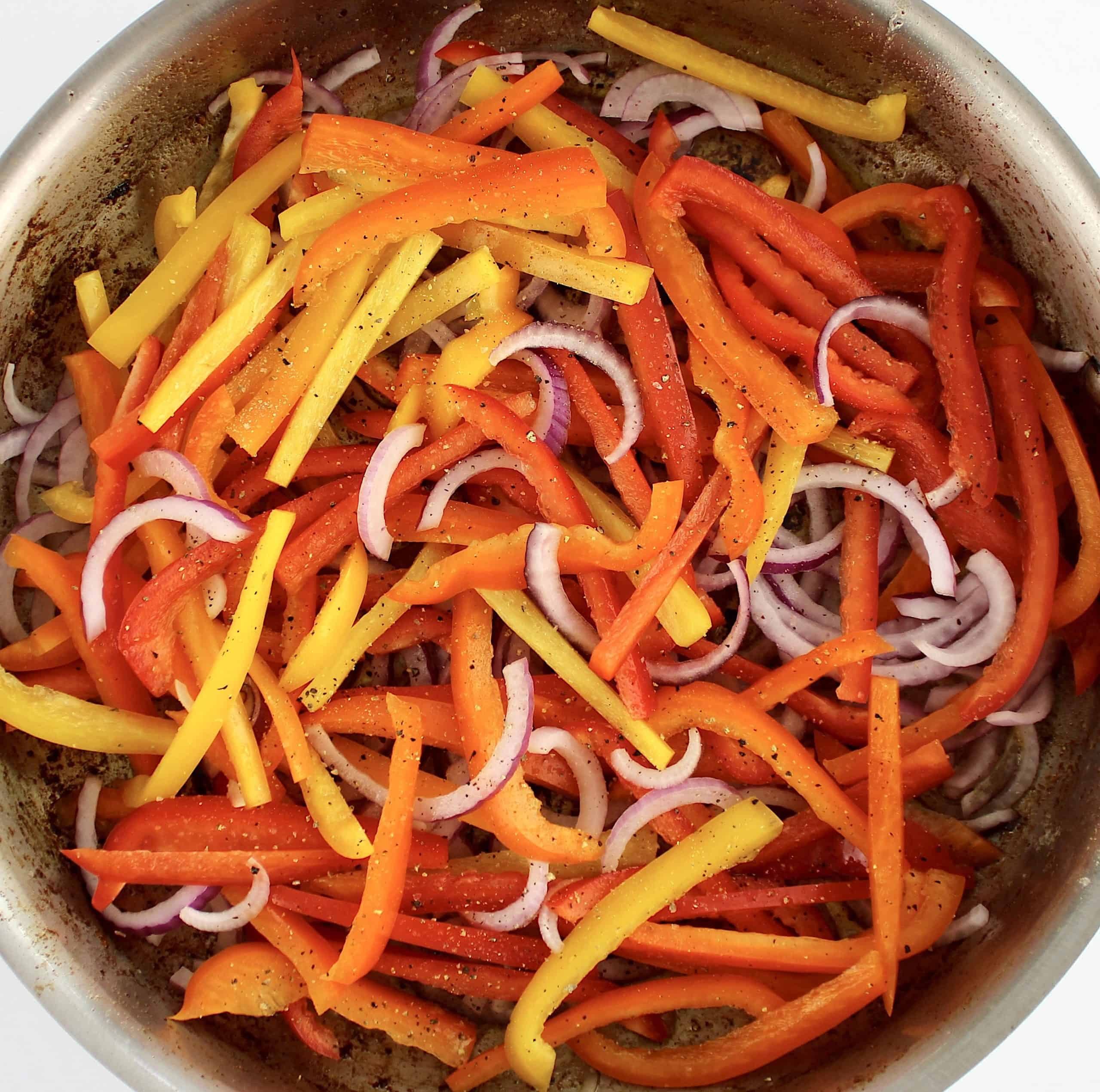 sliced red yellow and orange bell peppers and red onions in skillet uncooked