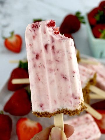 Keto Strawberry Cheesecake Popsicle being held up with bite missing