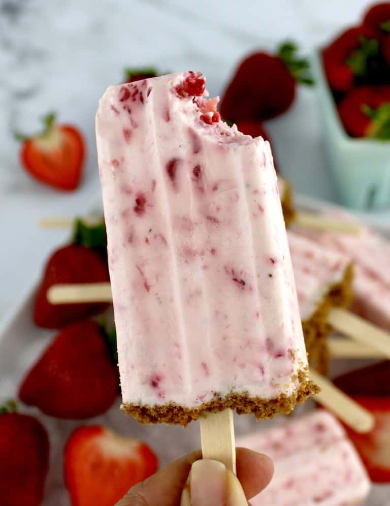 Keto Strawberry Cheesecake Popsicle being held up with bite missing
