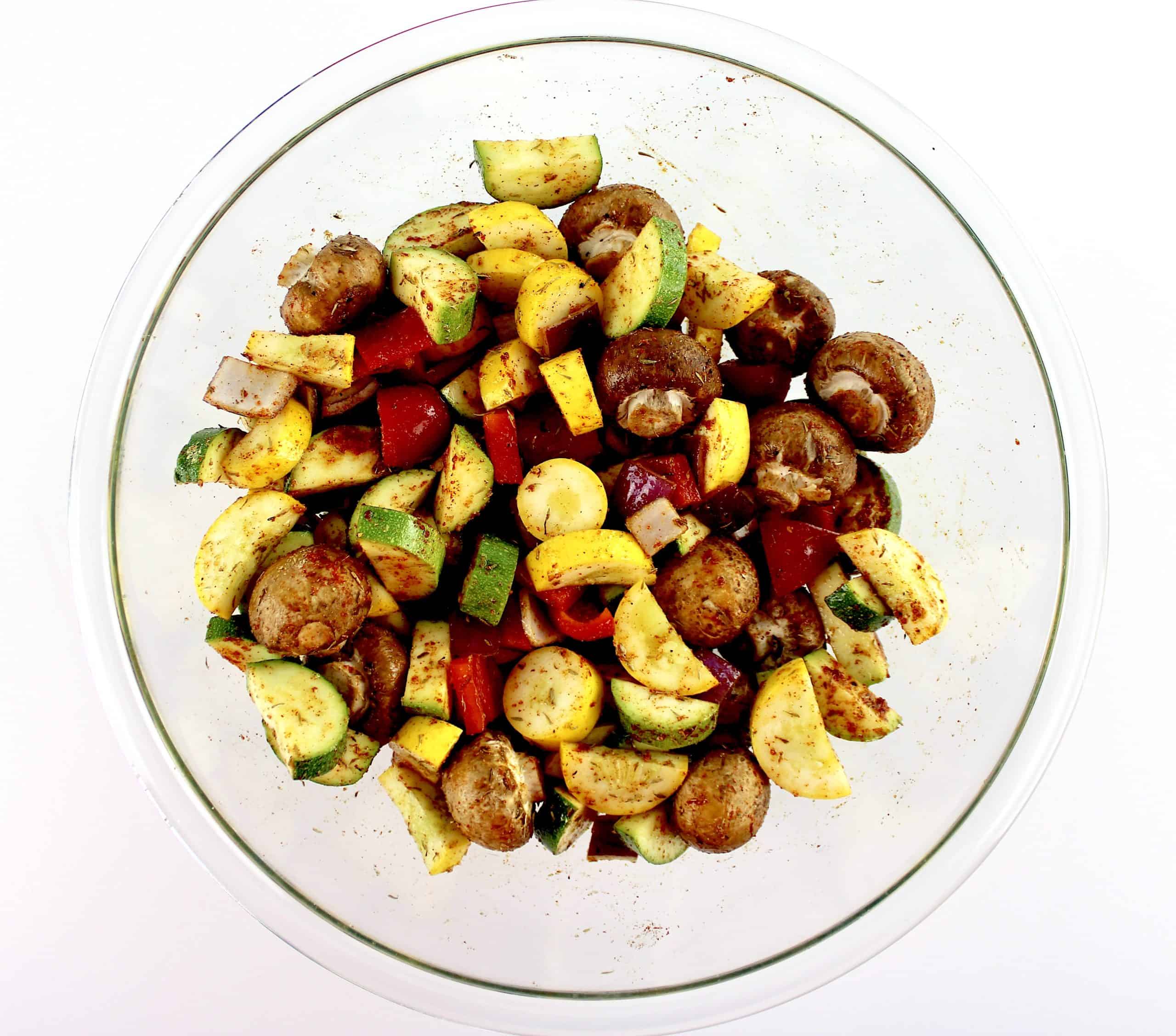 mixed Vegetables in glass bowl with spices herbs and olive oil over the top 