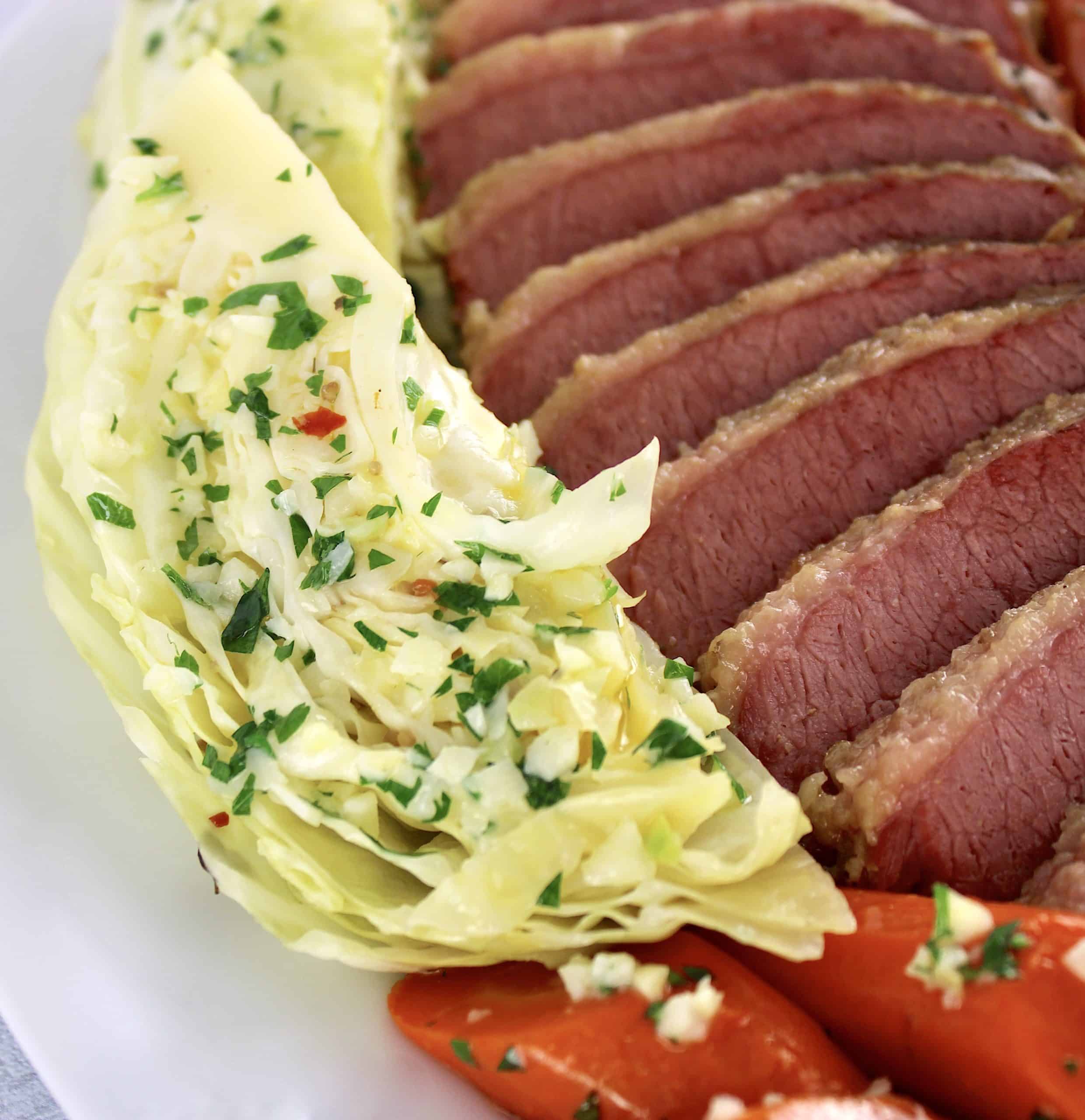 closeup of cabbage wedge sliced corned beef and carrots on white platter