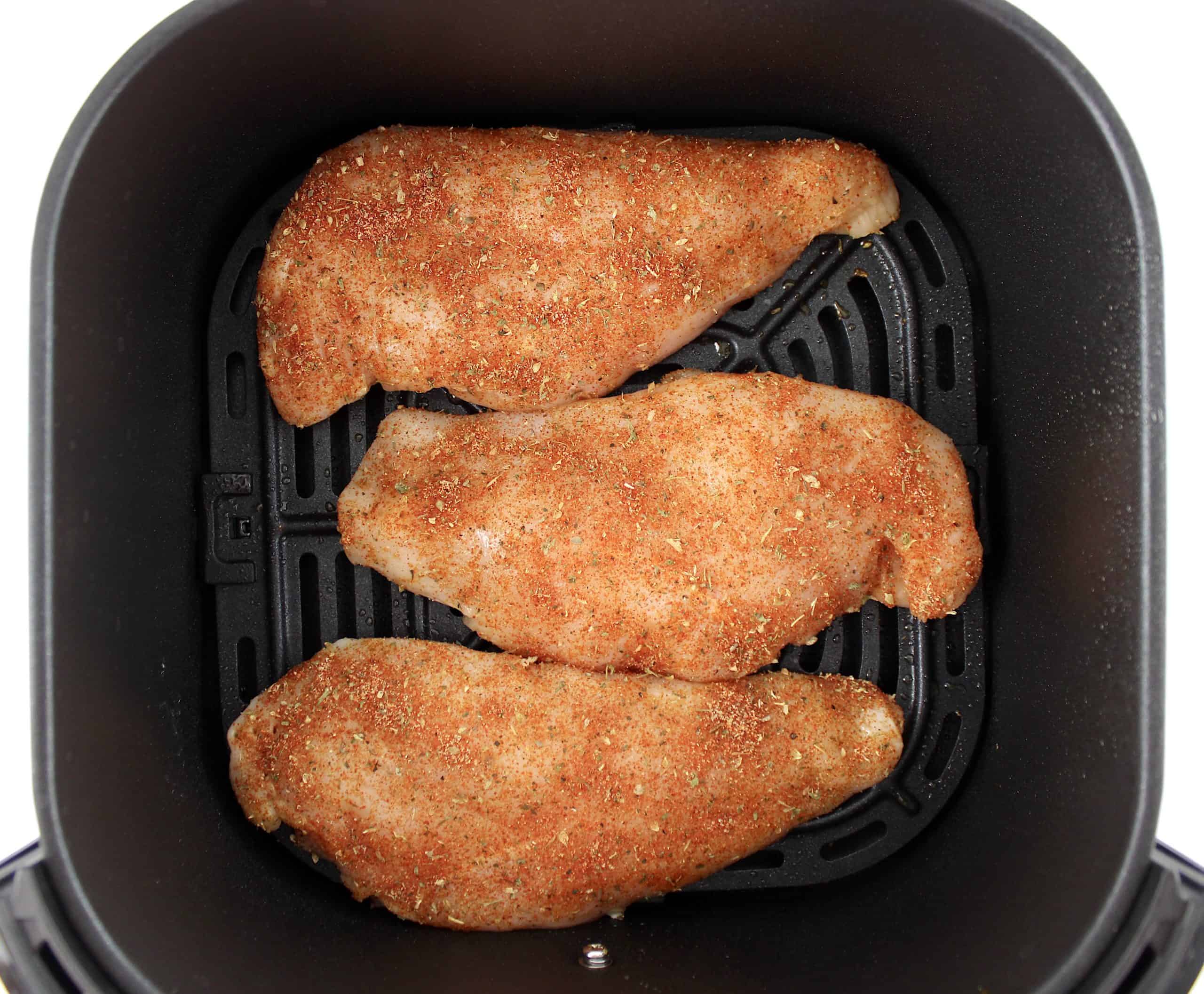 3 raw chicken breasts with seasonings in air fryer basket