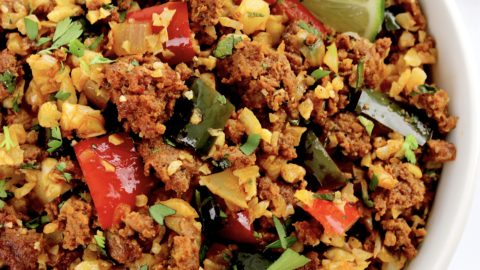 Chorizo and Pepper Cauliflower Rice inn white bowl with chopped cilantro and 2 lime slices on top