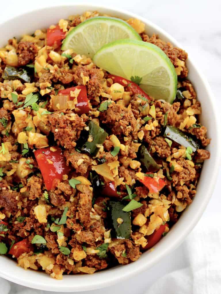 Chorizo and Pepper Cauliflower Rice inn white bowl with chopped cilantro and 2 lime slices on top