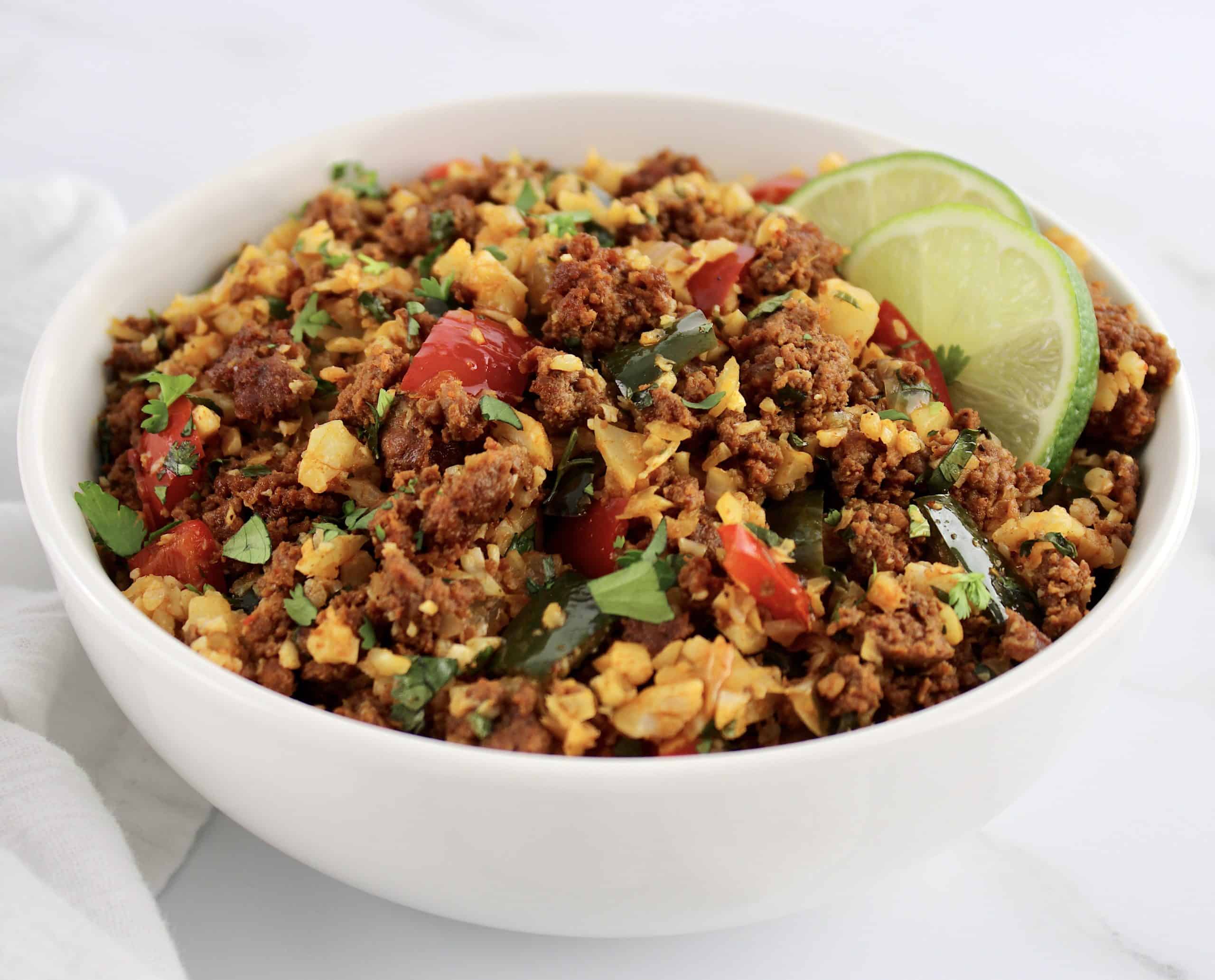 closeup of Chorizo and Pepper Cauliflower Rice in white bowl with 2 lime slices on side