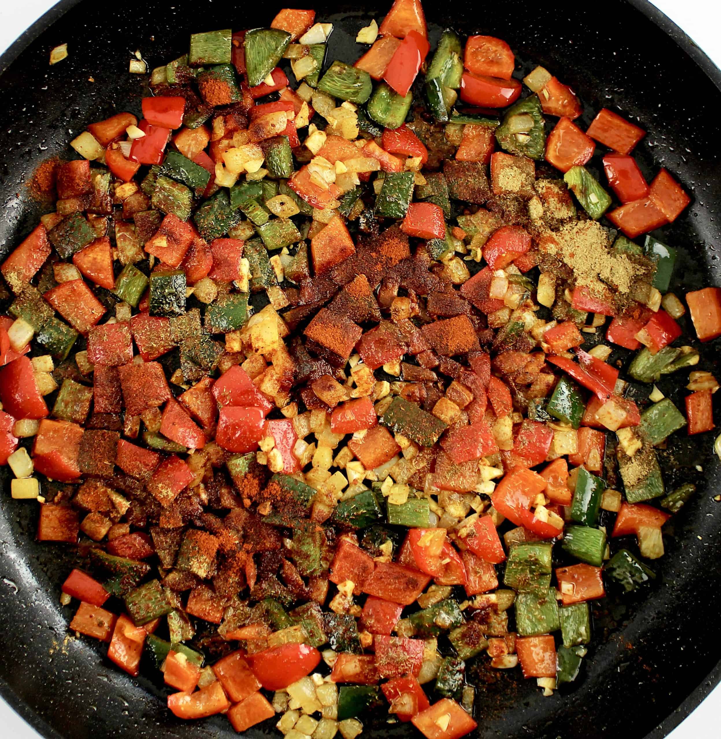 Sautéed peppers and onions with spices toasting in skillet